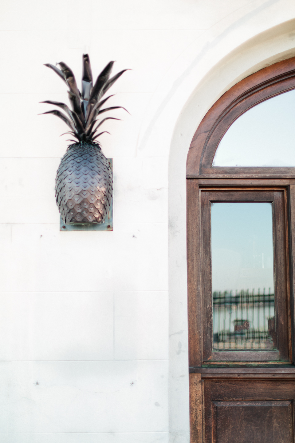 Picture of the outside of a building with wooden doors, glass panes, and an iron pineapple sconce.  East River Street in historic downtown Savannah, Georgia.
