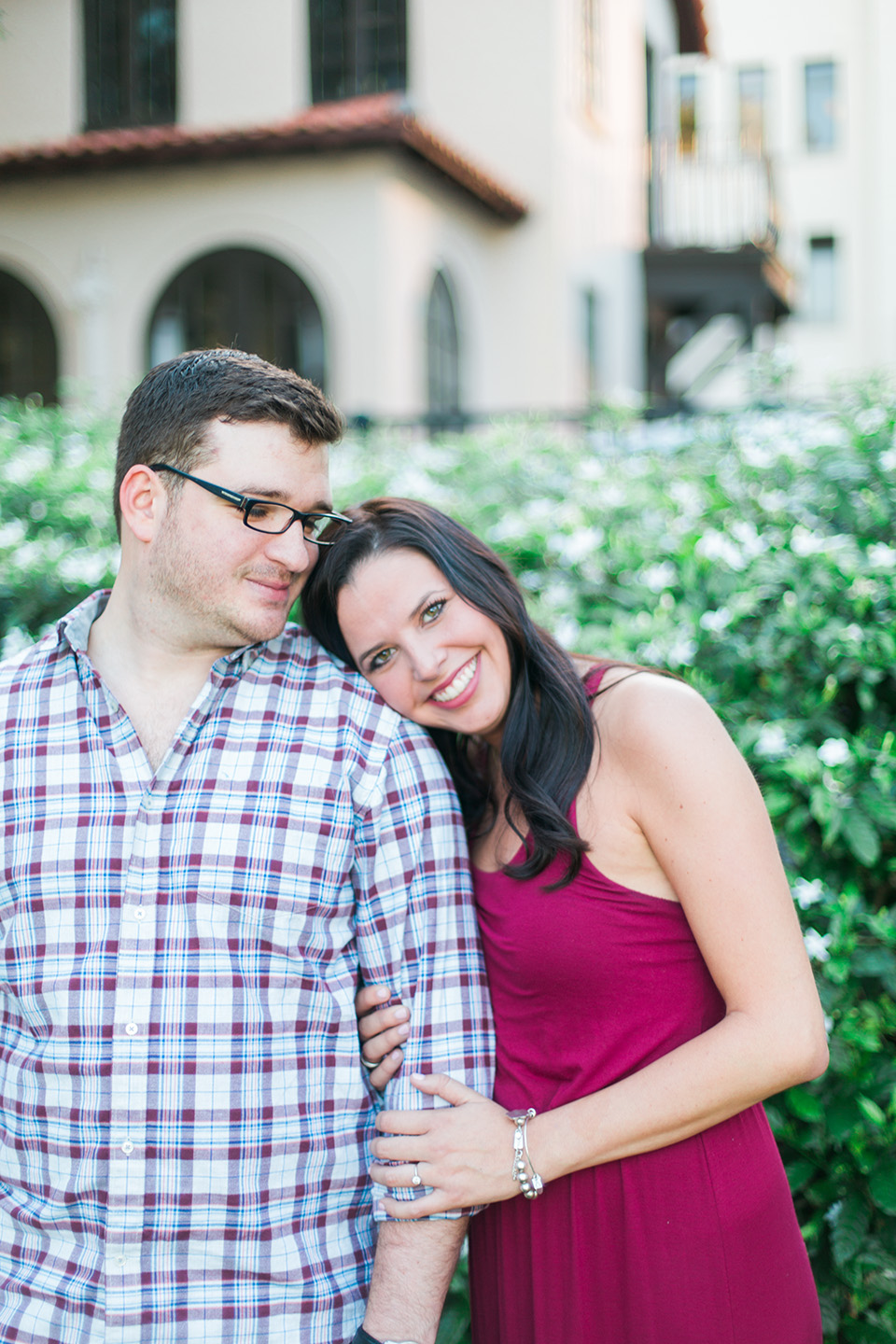 Image of an engaged couple, she is resting her head on his shoulder.  There is a black iron gate behind them in downtown Orlando, Florida.