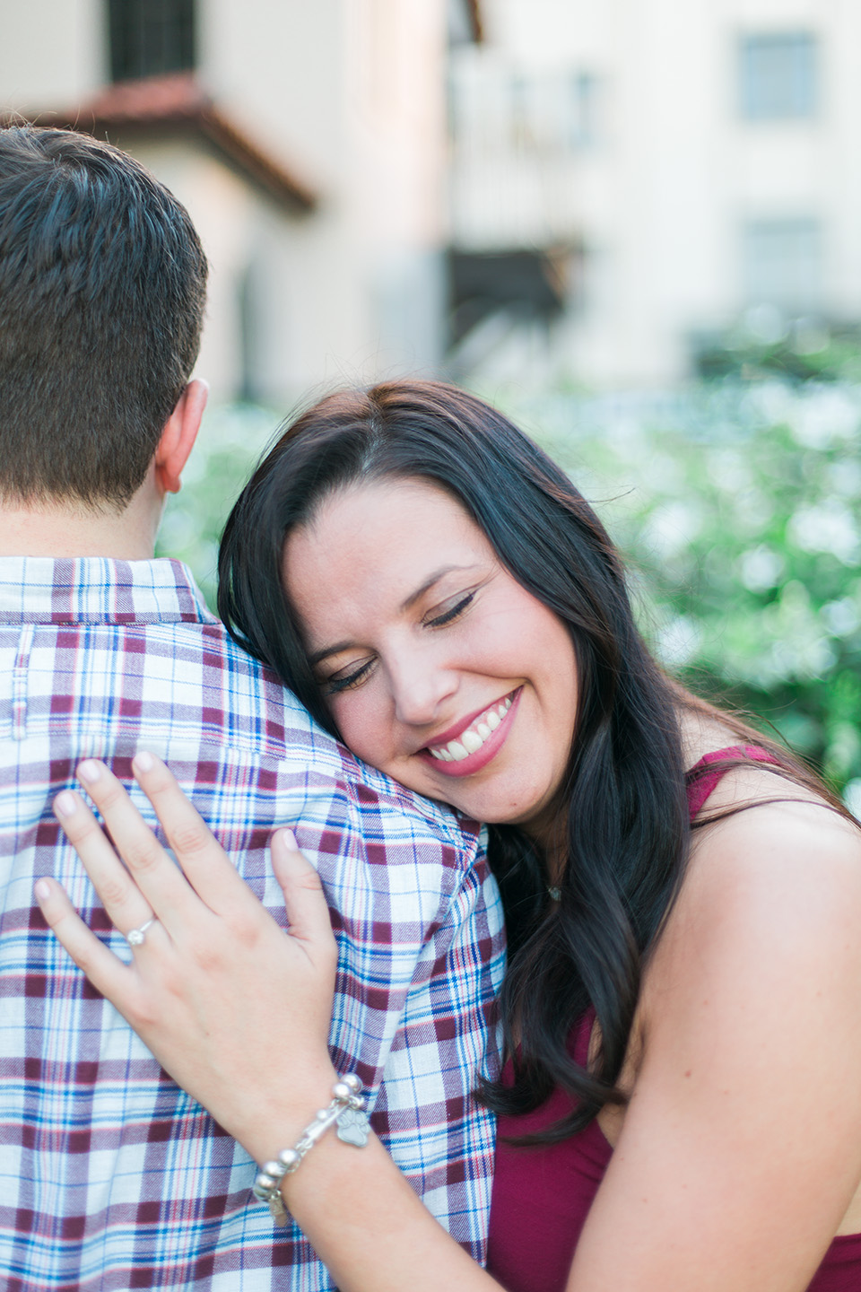 Image of an engaged couple in downtown Orlando, Florida.  The woman is closing her eyes and resting her head on her fiance's shoulder.  You can see her engagement ring on her left ring finger.