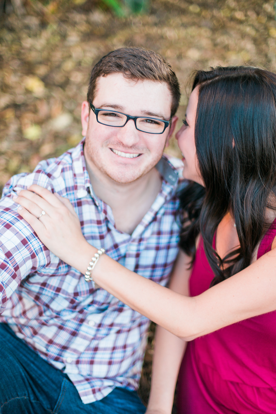 Image of an engaged couple in downtown Orlando, Florida.  The man is looking into the camera, smiling, while the woman is embracing him and whispering into his ear.