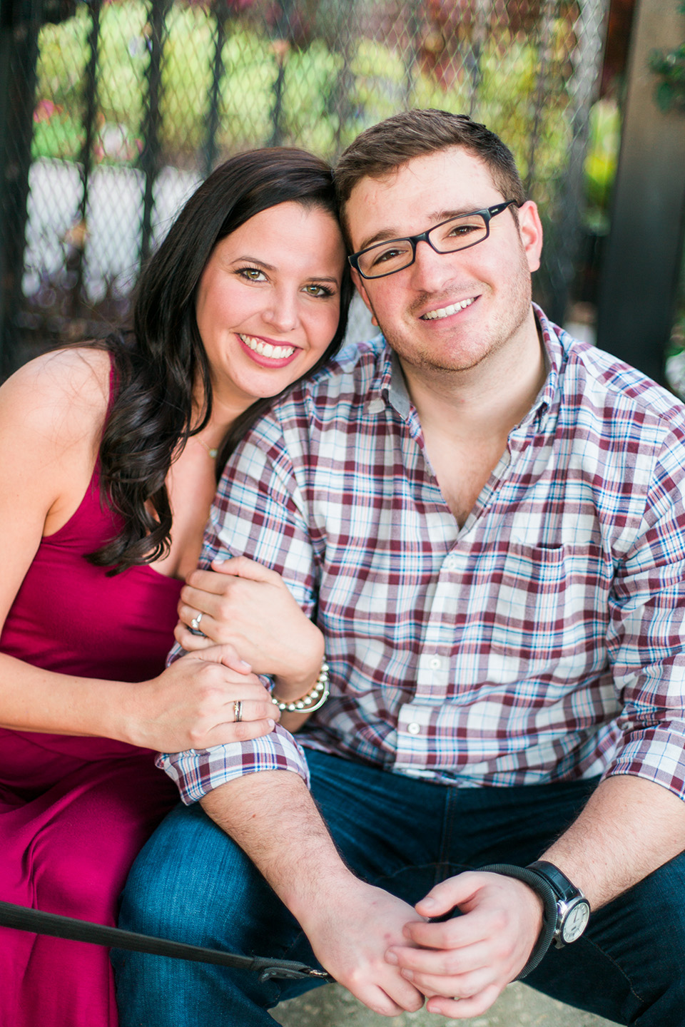 Picture of an engaged couple looking into the camera and smiling.  They are sitting in front of a gate on some steps in downtown Orlando, Florida