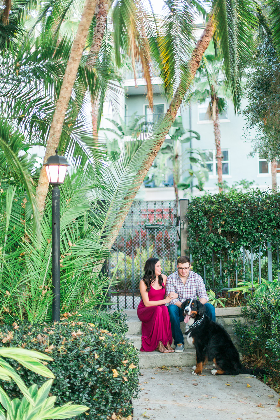 Image of a couple and their dog sitting on steps downtown Orlando, Florida, in front of a gated apartment complex.