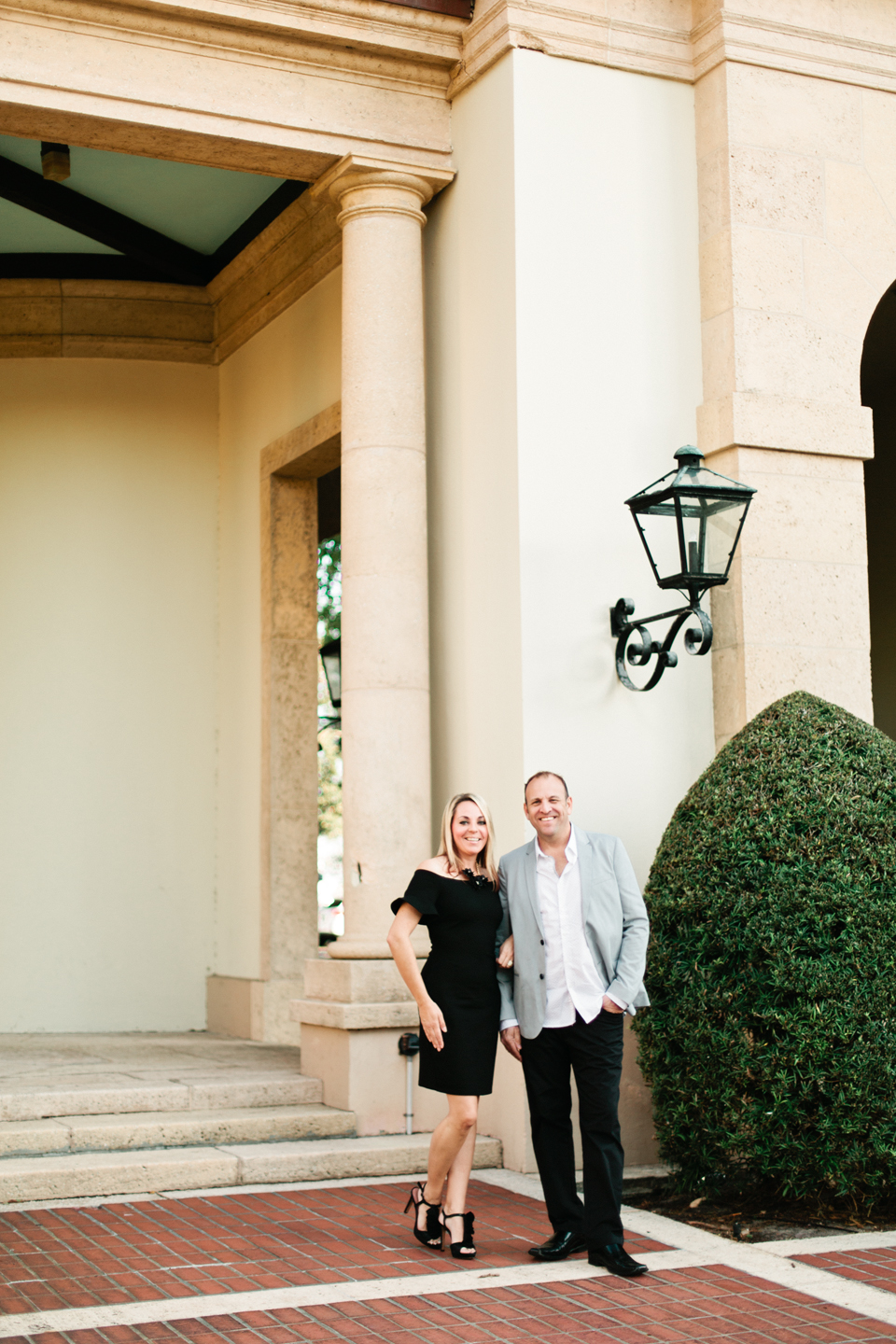 Picture of a couple standing in front of the Museum of Fine Arts downtown St. Pete.  The woman is wearing a short black dress with ruffle sleeves.  The man is wearing dress pants and a sportscoat.