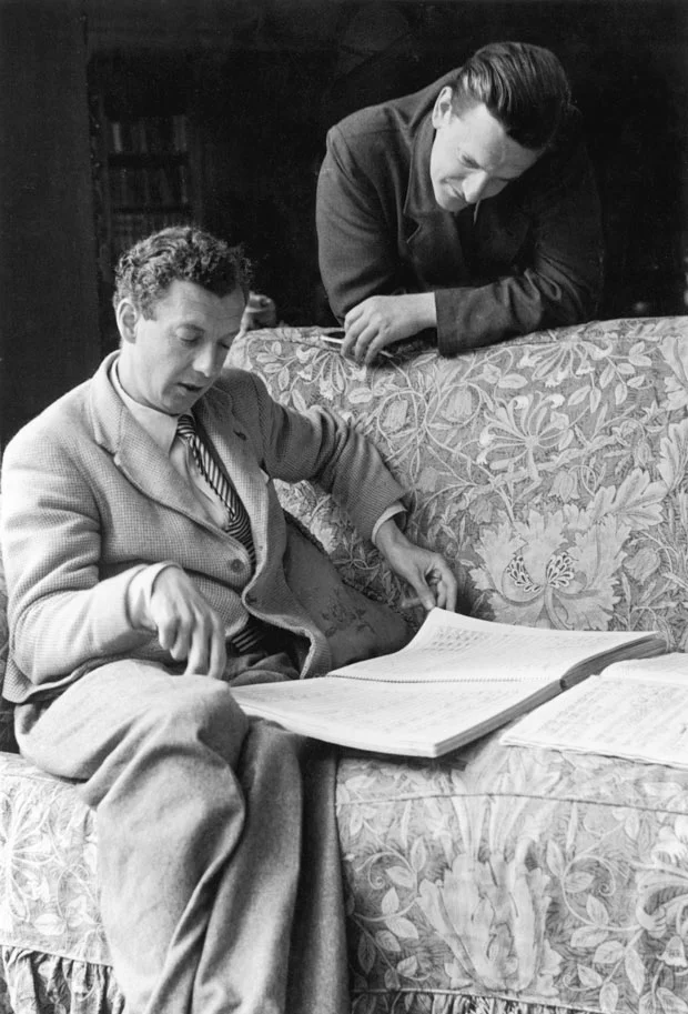 Britten studying music on a couch, with Peter Pears studying over his shoulder