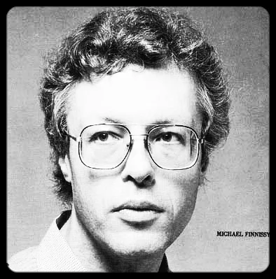 Finnissy looking serious and off to the side of the camera angle. He has short wavy hair and large write-rimmed glasses.