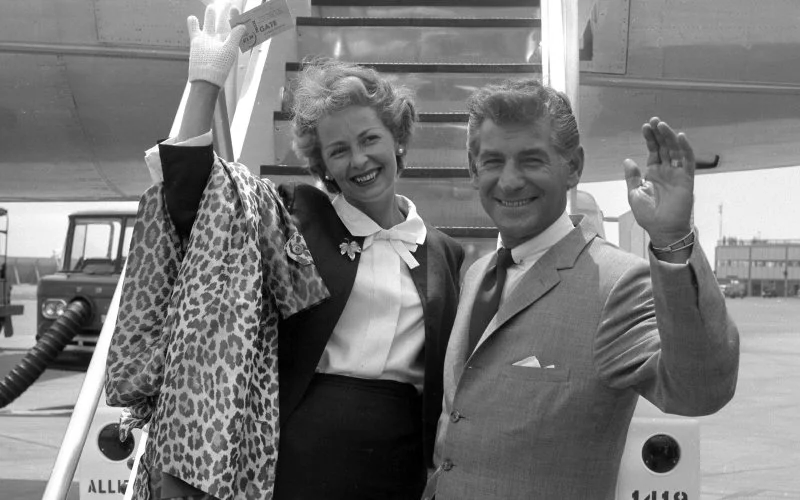 Bernstein and his wife having just disembarked from a plane, wave and smile for the camera