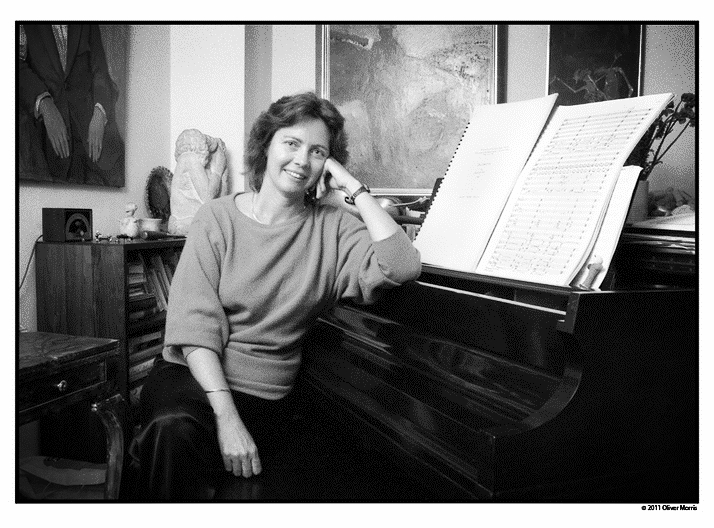 Zwilich in a baggy sweater with her elbow on a closed grand piano.