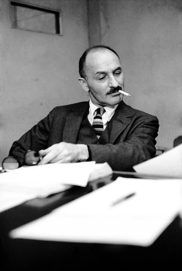 Mark Blitzstein studying sheet music on a piano, his eyes cocked and a cigarette in his mouth