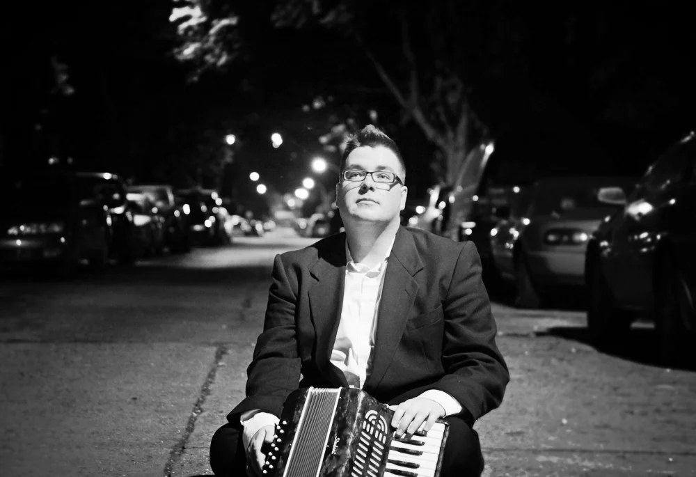 Michael Park sitting under a streetlight with his accordion.
