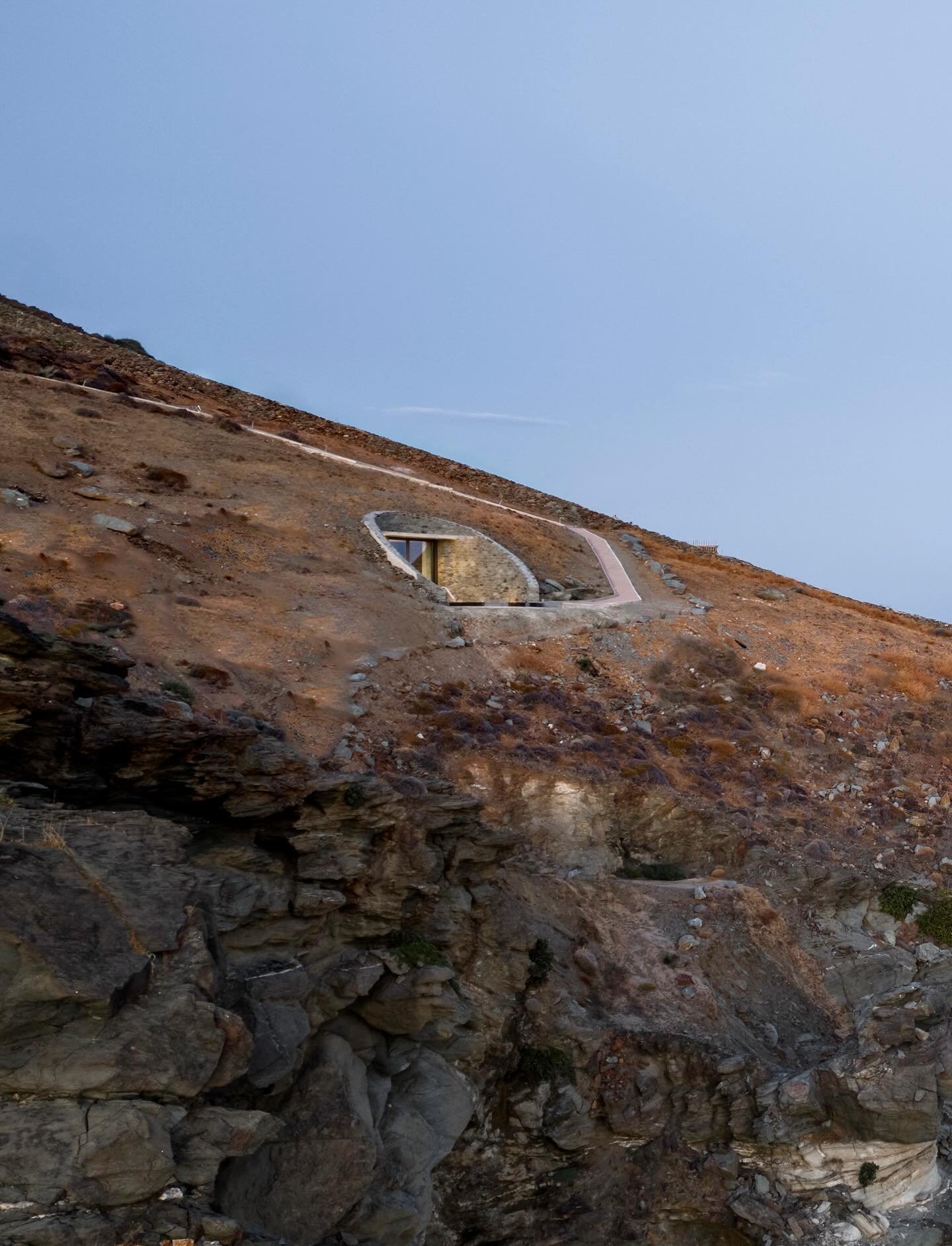 On the island of Syros, Olen unfolds like a quiet composition facing the Aegean Sea. Set on a steep south-facing slope, the resort follows the natural amphitheater of the land. Architecture is shaped by terrain, light, and horizon, creating a layered