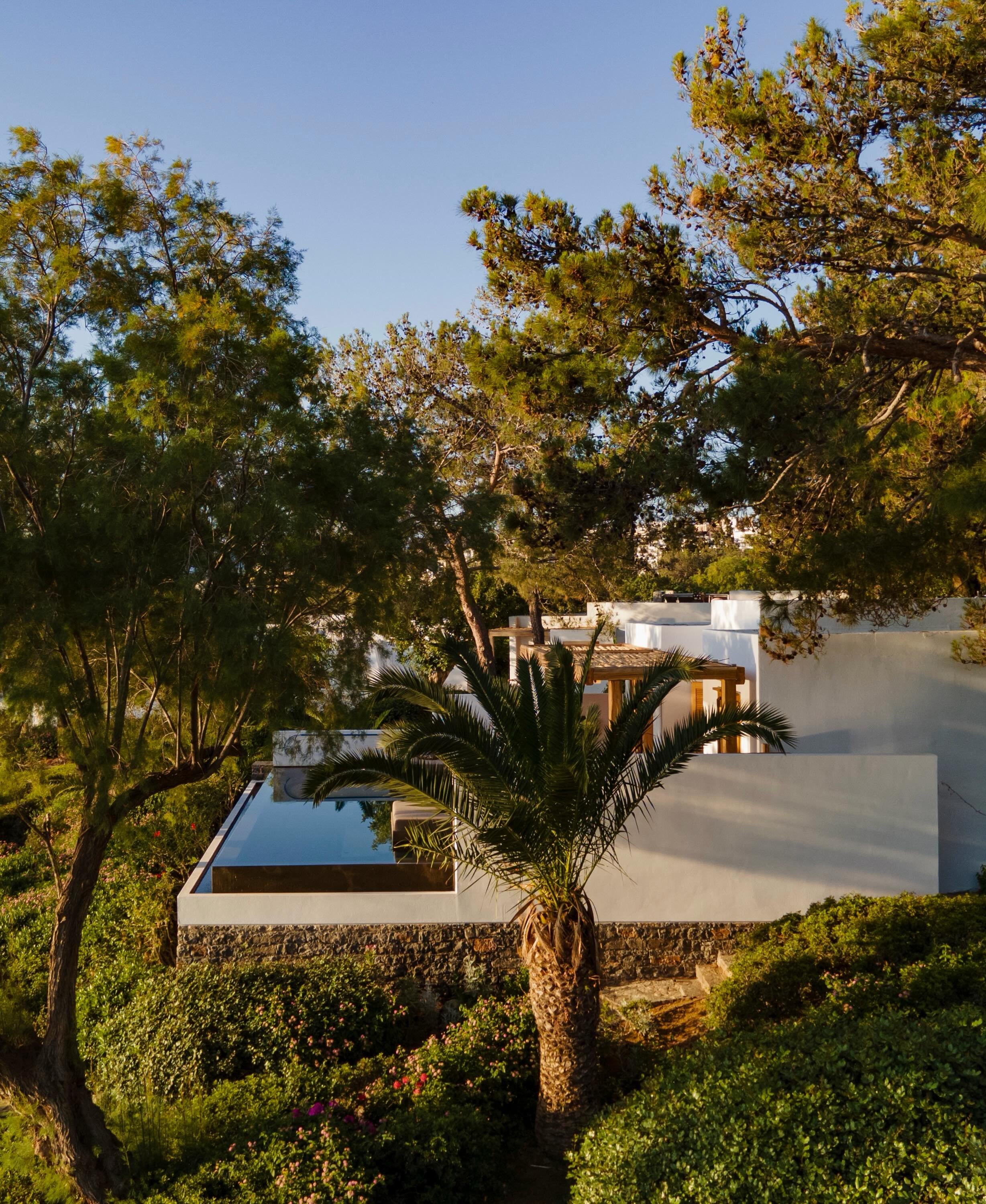 On the coast of eastern Crete, Minos Beach Art Hotel unfolds along a peninsula shaped by pine trees, rocky inlets, and quiet bays. The architecture is low and dispersed, allowing the natural topography to remain dominant while whitewashed bungalows a