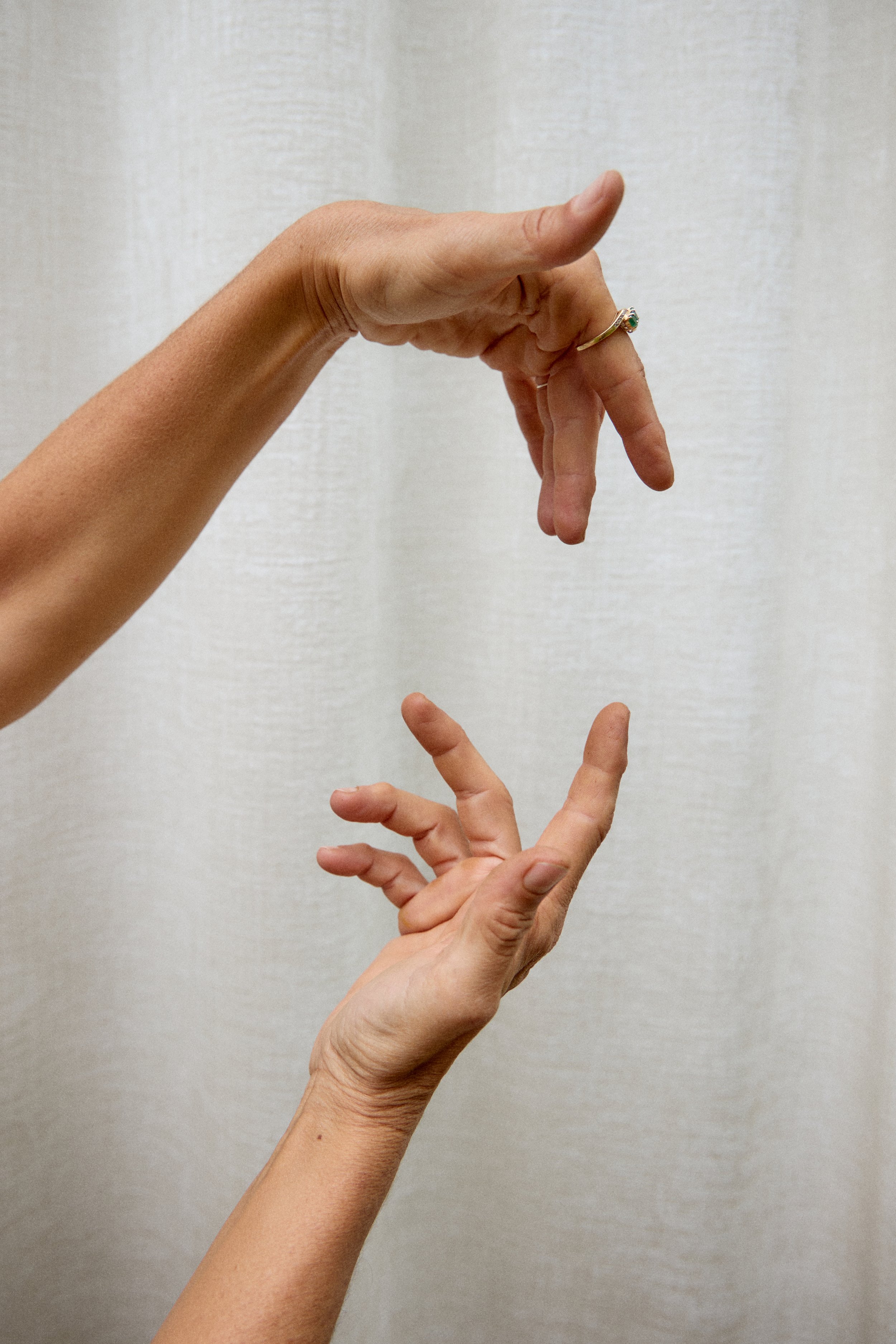 Two hands with fingers positioned in a gesture, one above the other, against a neutral background.