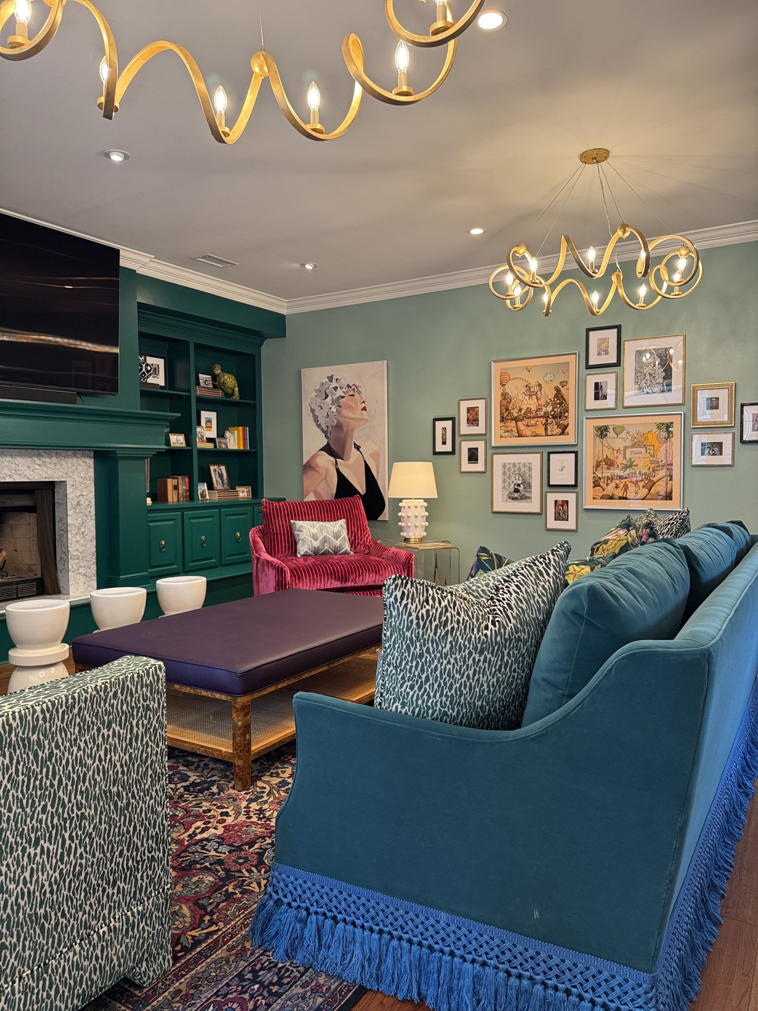 Wide view of an eclectic living room with green walls, blue and red seating, and brass chandeliers