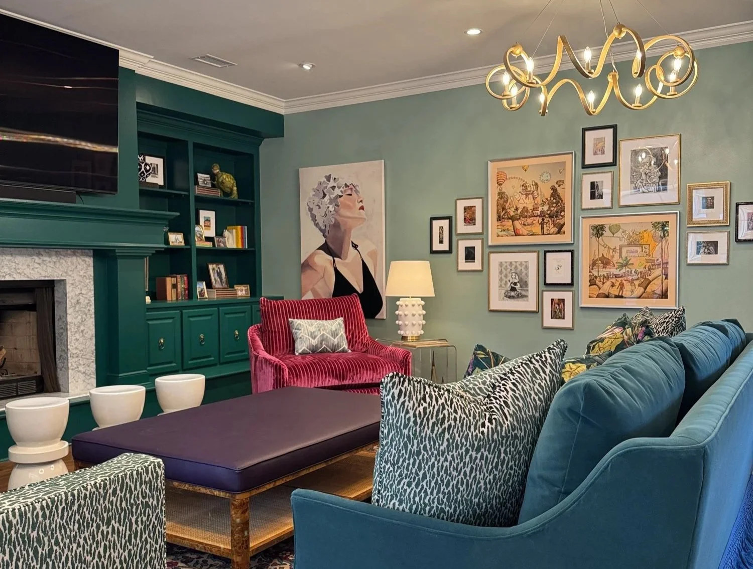 A teal living room with a fringed sofa, patterned accent chairs, and a gallery wall