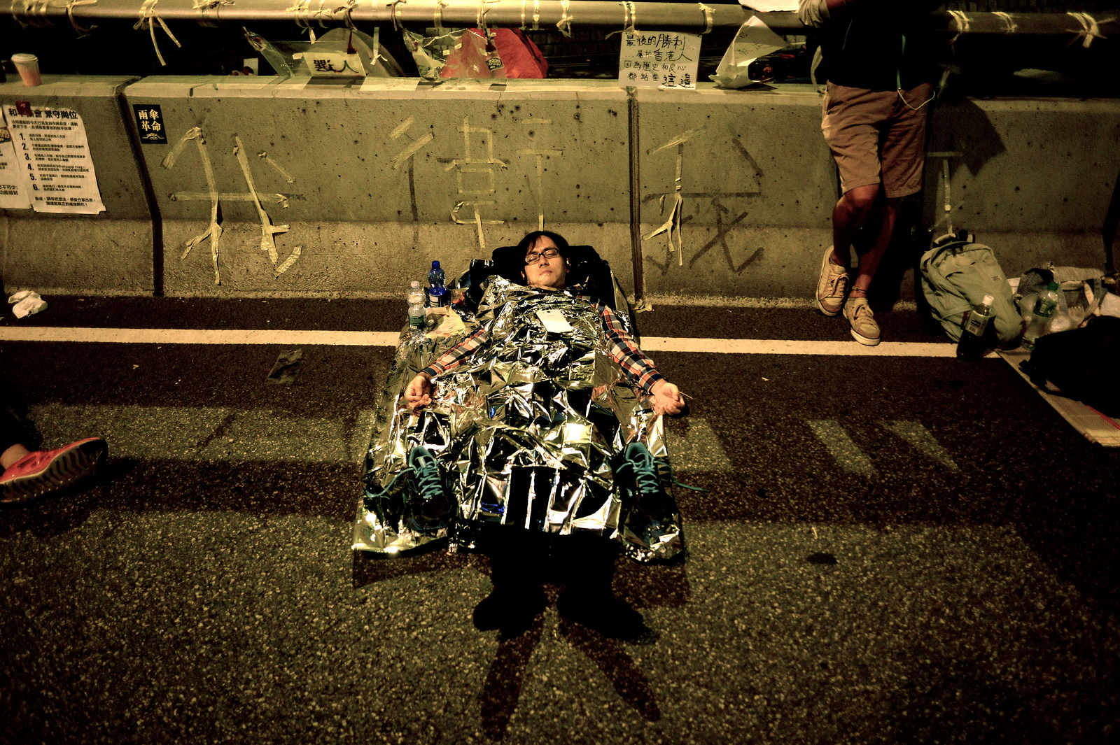 An occupier sleeps under a thin reflective sheet on the Admiralty flyover. Behind him, spelled out in tape, is the slogan 我衛我, which roughly translates to "I Protect Myself".