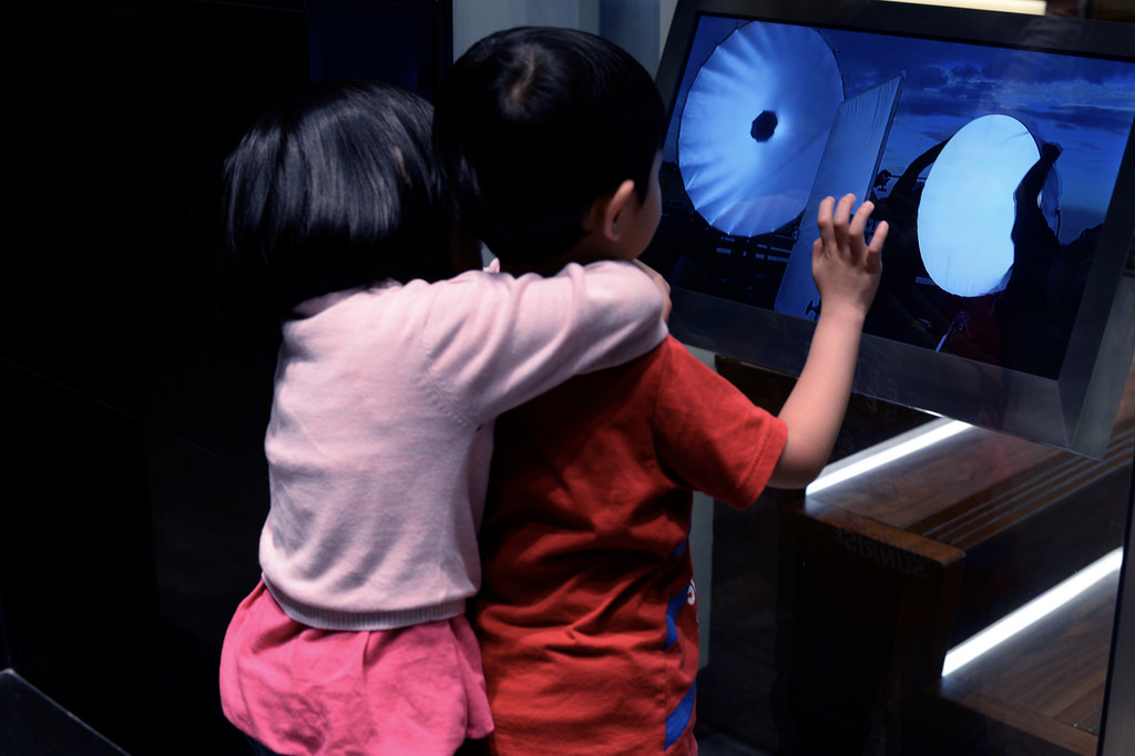 two children are transfixed by the cold cryptic shapes on a screen in a shop window.