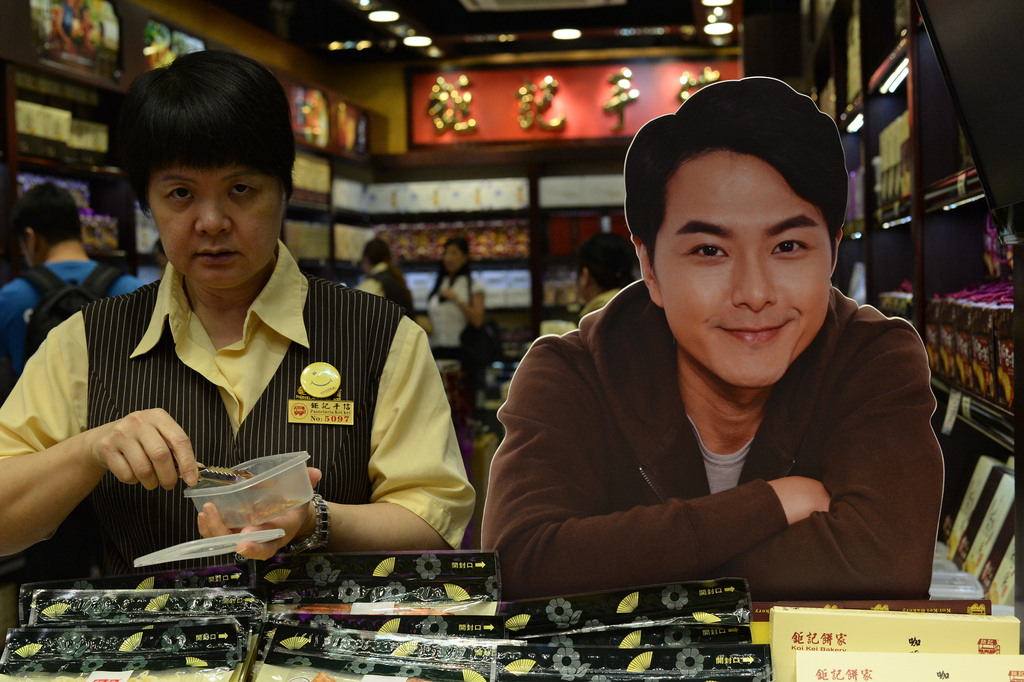 a saleswoman deep into her shift at a koi kei macanese bakery location in causeway bay rubs shoulders with a perpetually cheerful promotional cutout. 