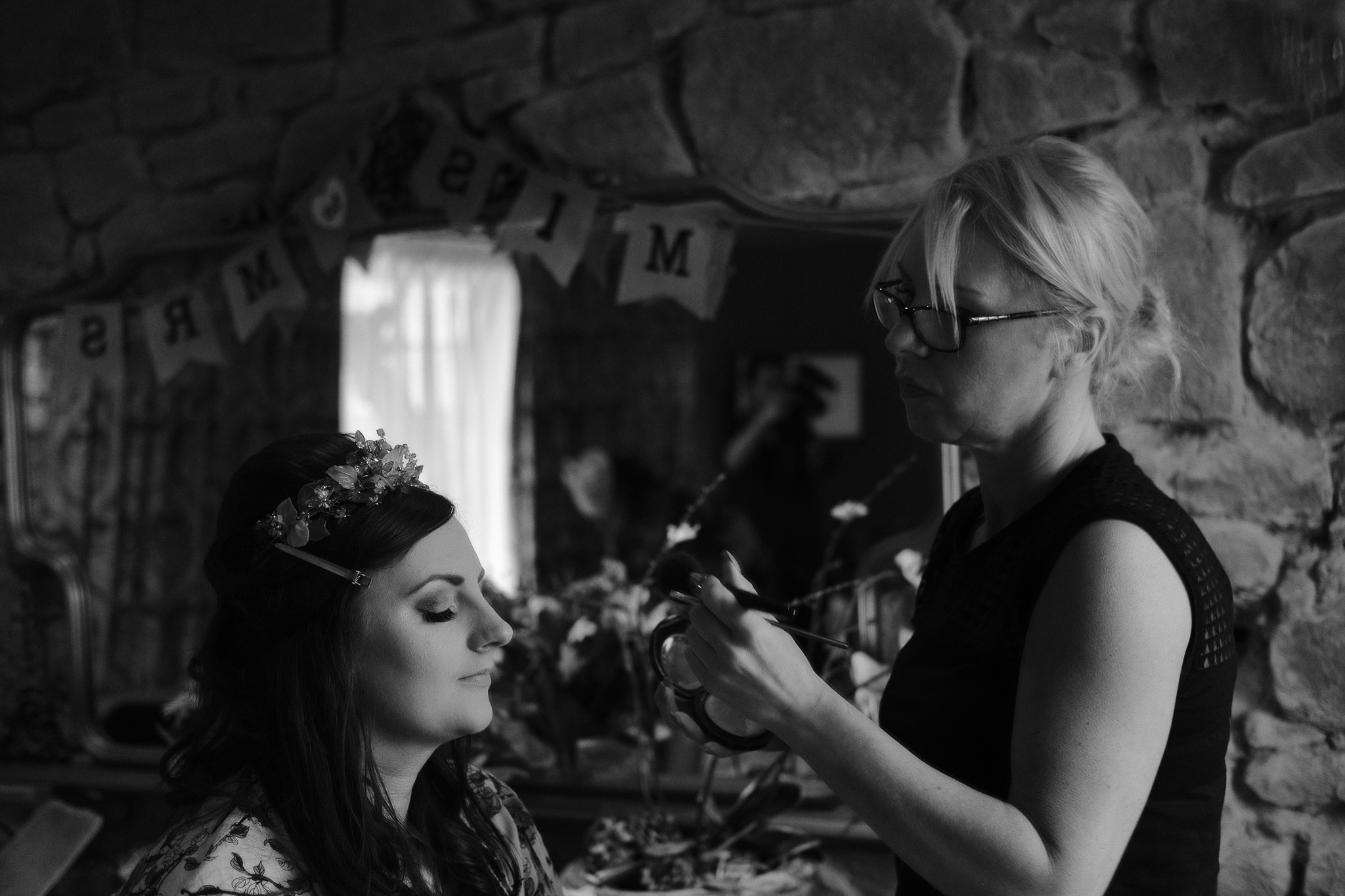 A black and white photograph of Tanya has her bridal makeup applied at Newton Hall, Northumberland by Barry Forshaw