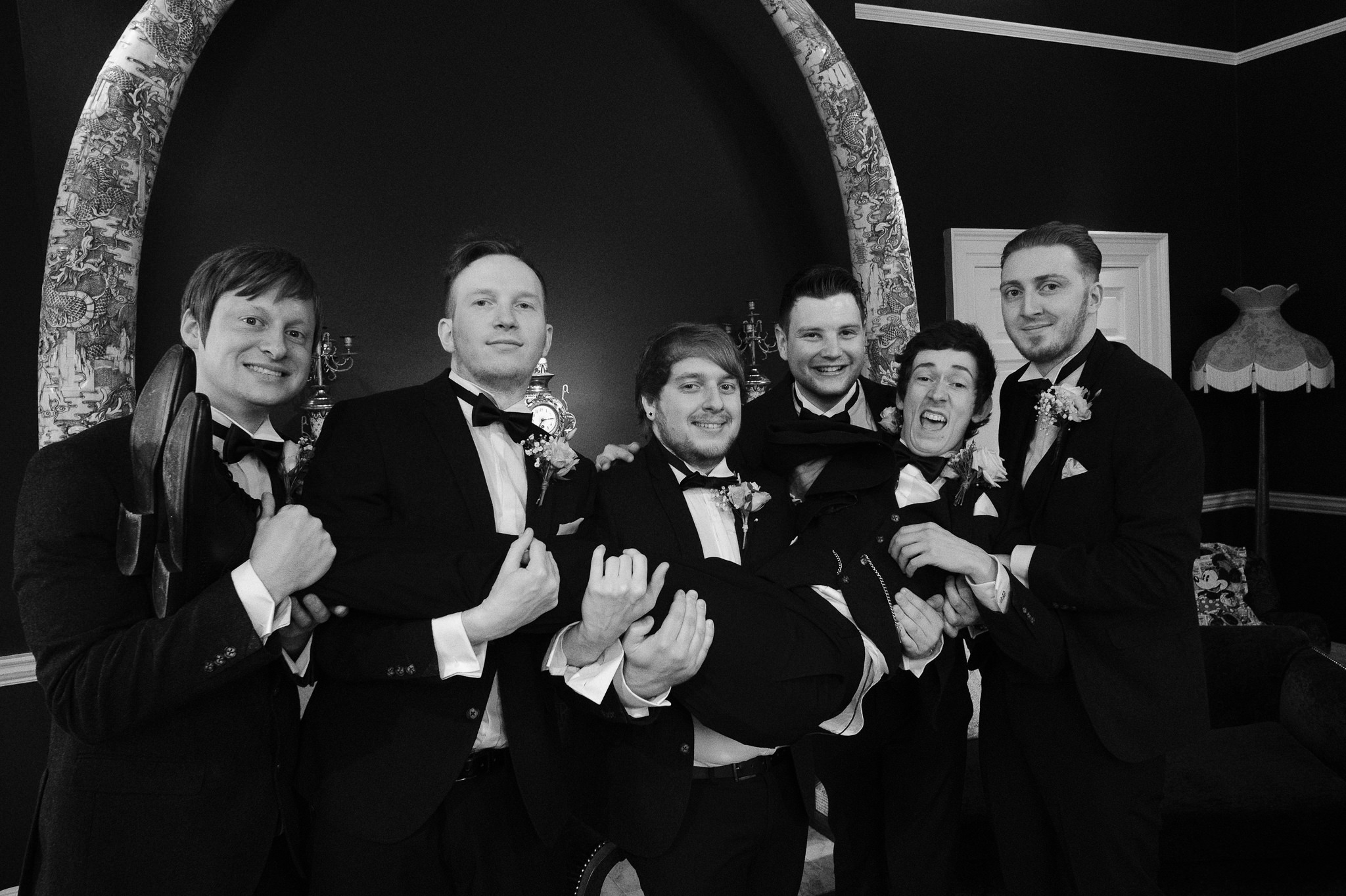 A black and white photo of the groomsmen holding the groom at Newton Hall, Northumberland by Barry Forshaw
