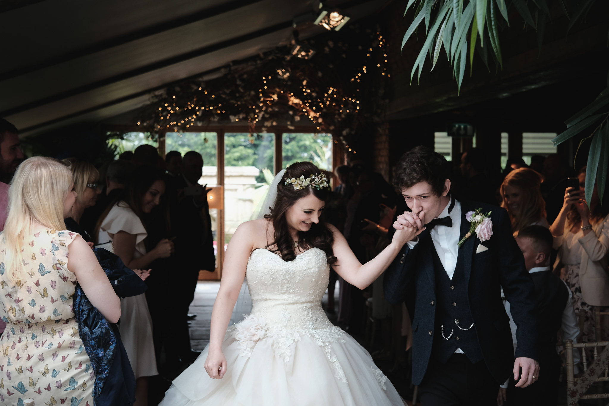 The groom kisses the brides' hand as they leave the wedding ceremony at Newton Hall, Northumberland by Barry Forshaw