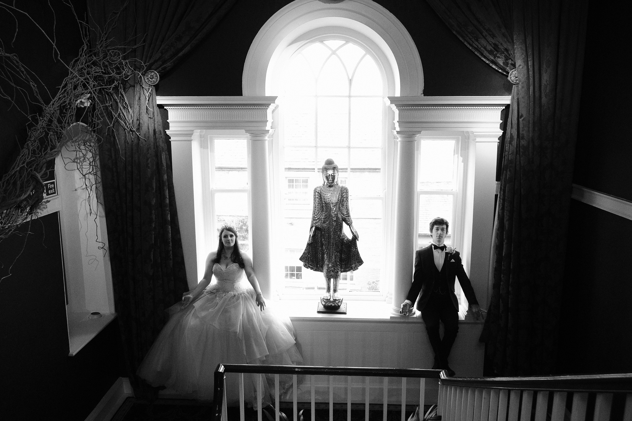 A black and white photo of the bride and groom sitting in a large window tapping their inner spirituality at Newton Hall, Northumberland by Barry Forshaw