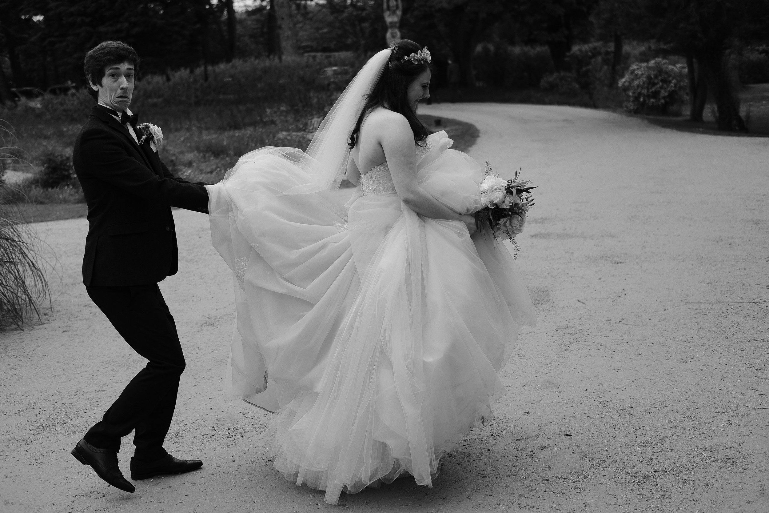 The groom holds up the brides dress and makes a funny face at Newton Hall Northumberland by Barry Forshaw