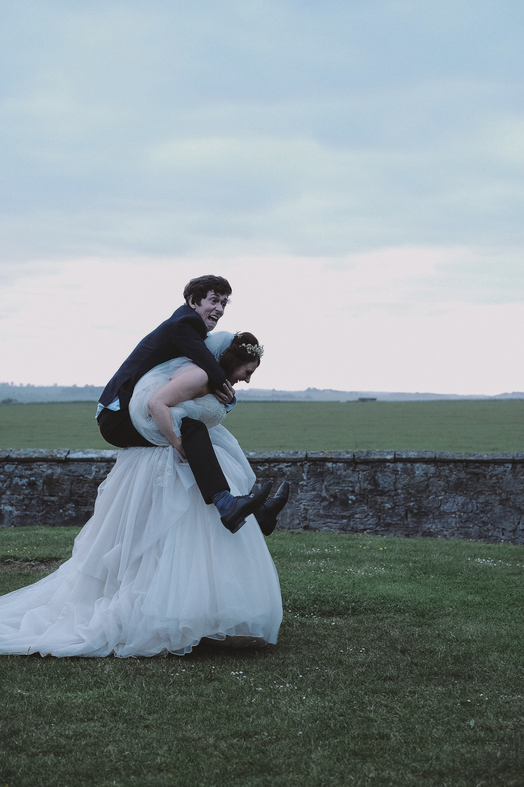 The bride gives the groom a piggy back at Newton Hall Northumberland by Barry Forshaw