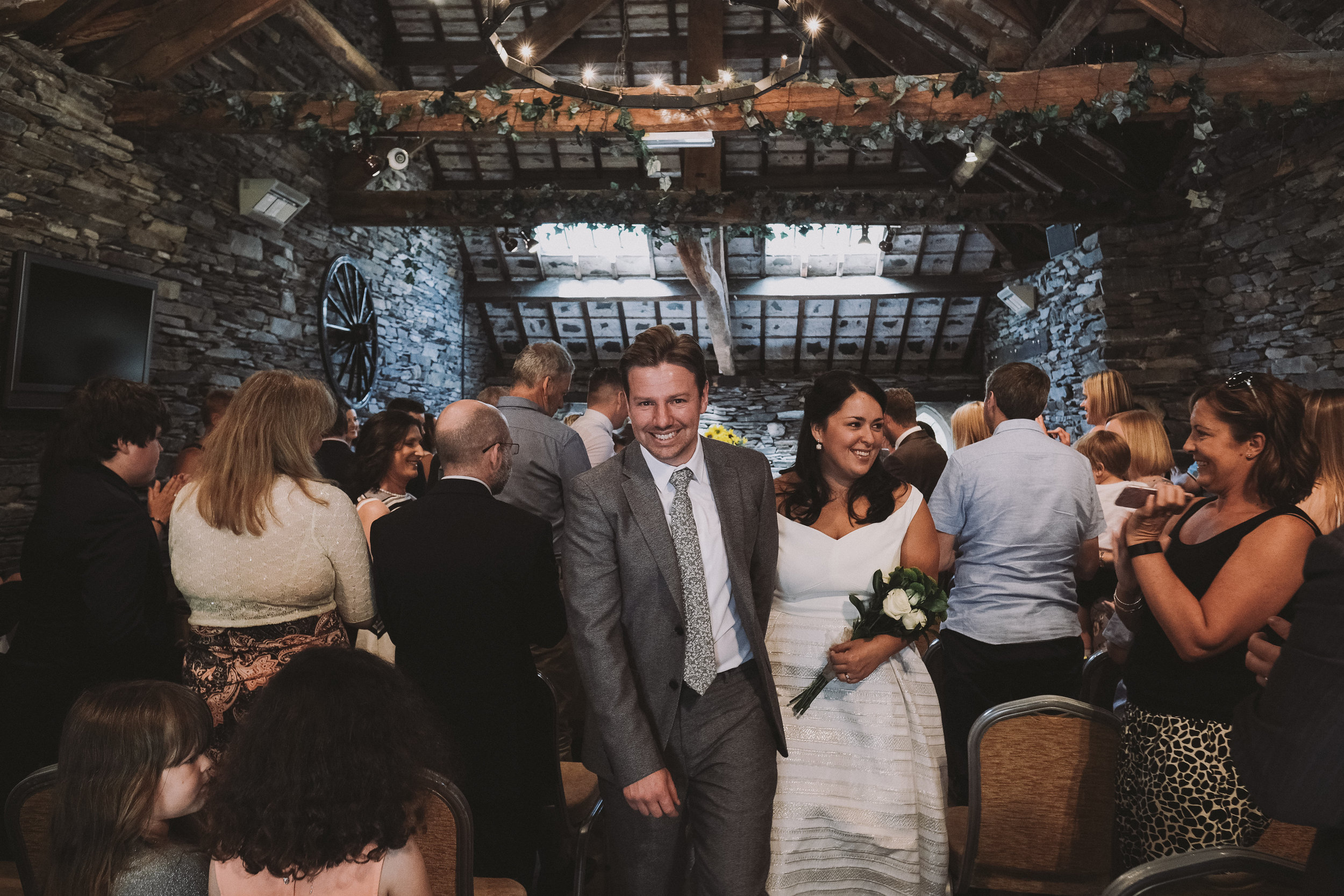 The bride and groom smile as they leave the ceremony at Julia and Darren's Lake District wedding by Barry Forshaw