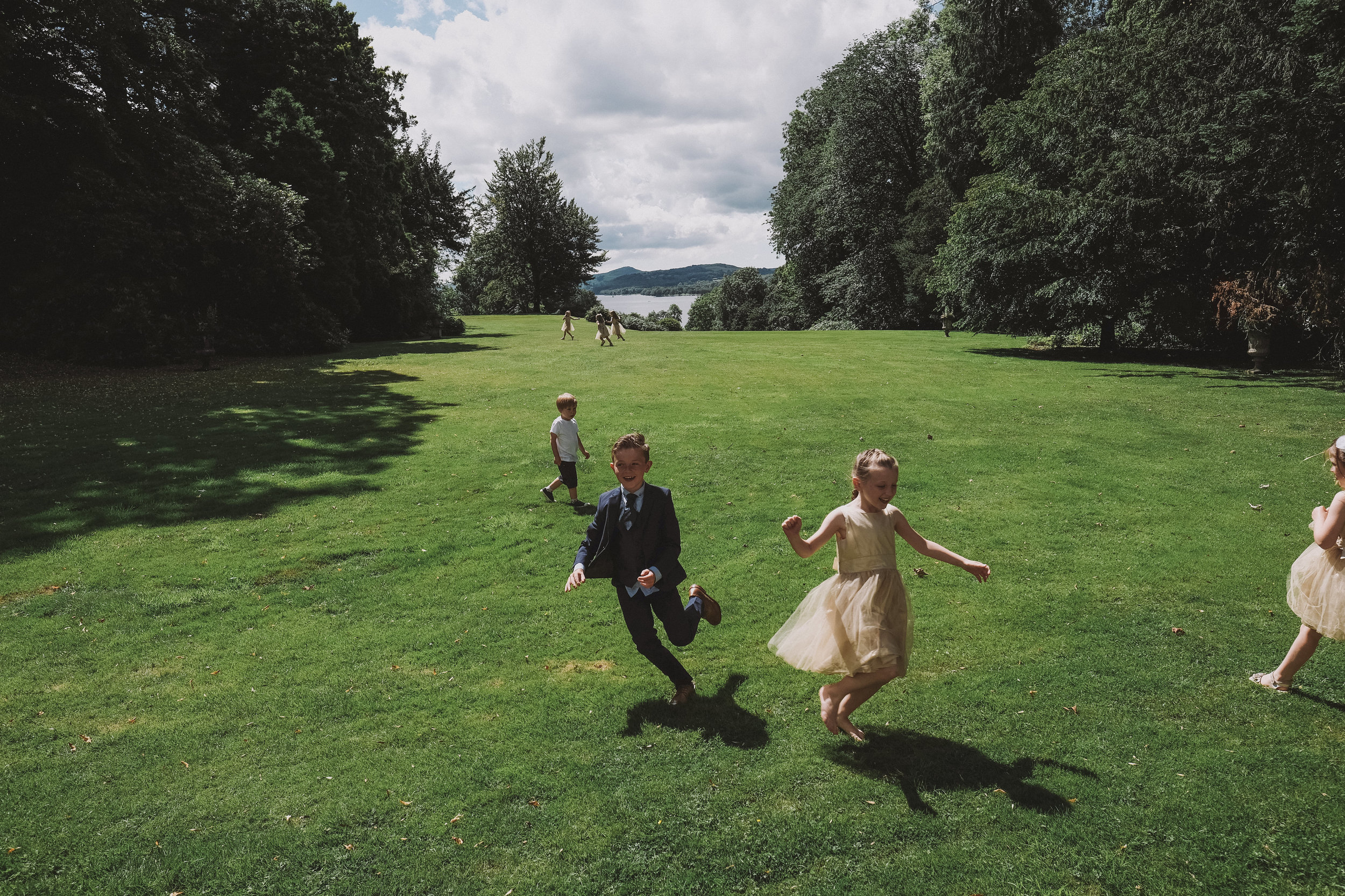 Silly play by children in the grounds of Monk Coniston Hall with Coniston Water in the background at Julia and Darren's Lake District wedding by Barry Forshaw