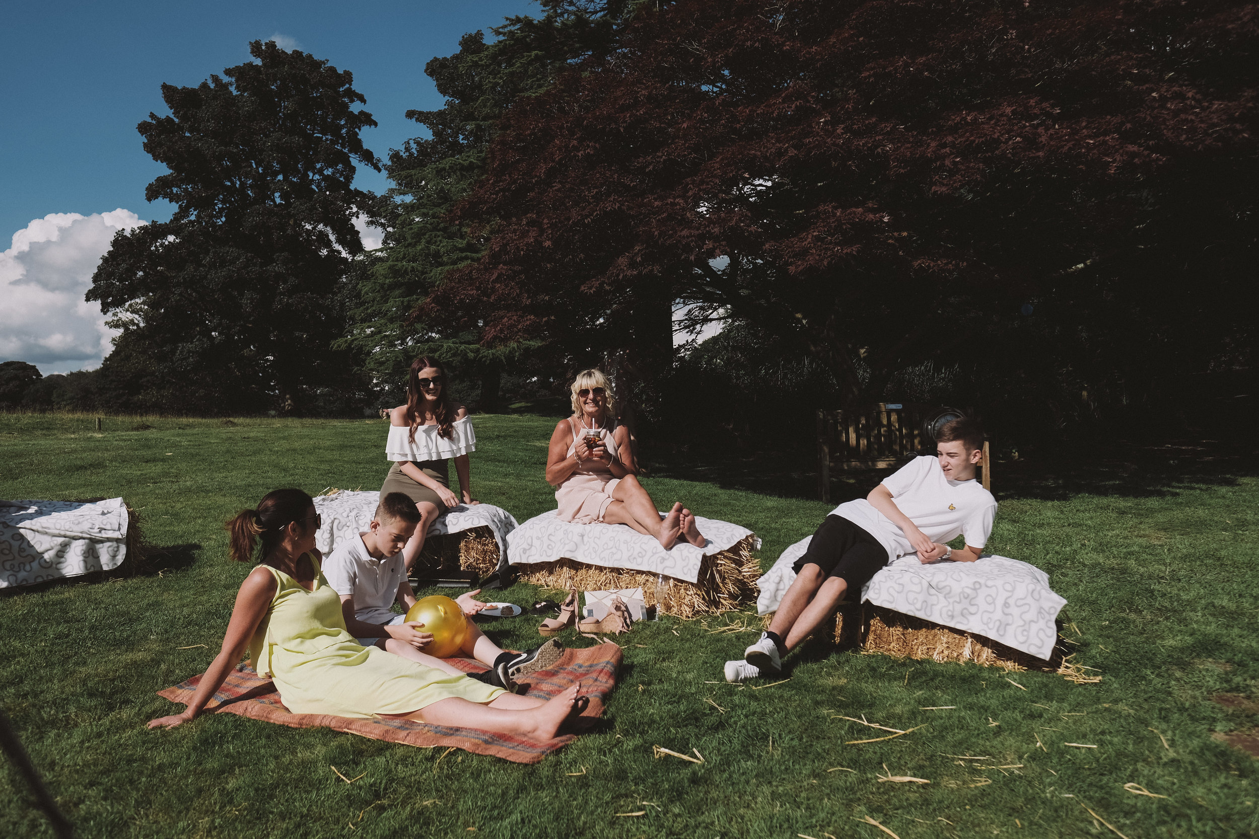 Wedding guests sit on hay bales at Julia and Darren's Lake District wedding by Barry Forshaw