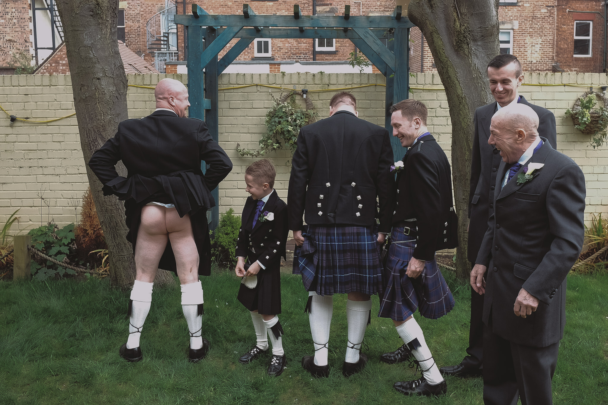 A groomsman lifts up his kilt as the rest of the groomsmen look on and laugh
