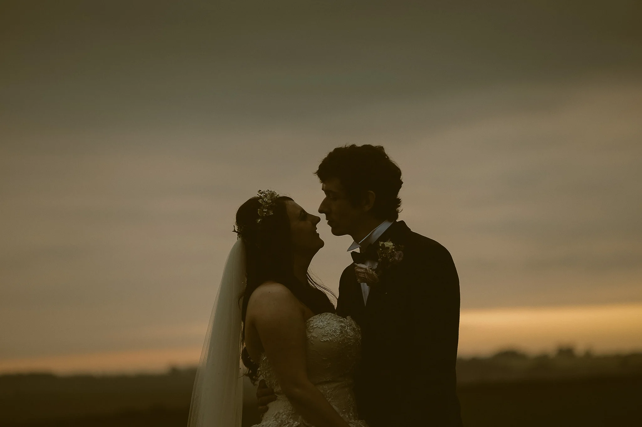 Bride and groom look into each others eyes with a golden sunset behind