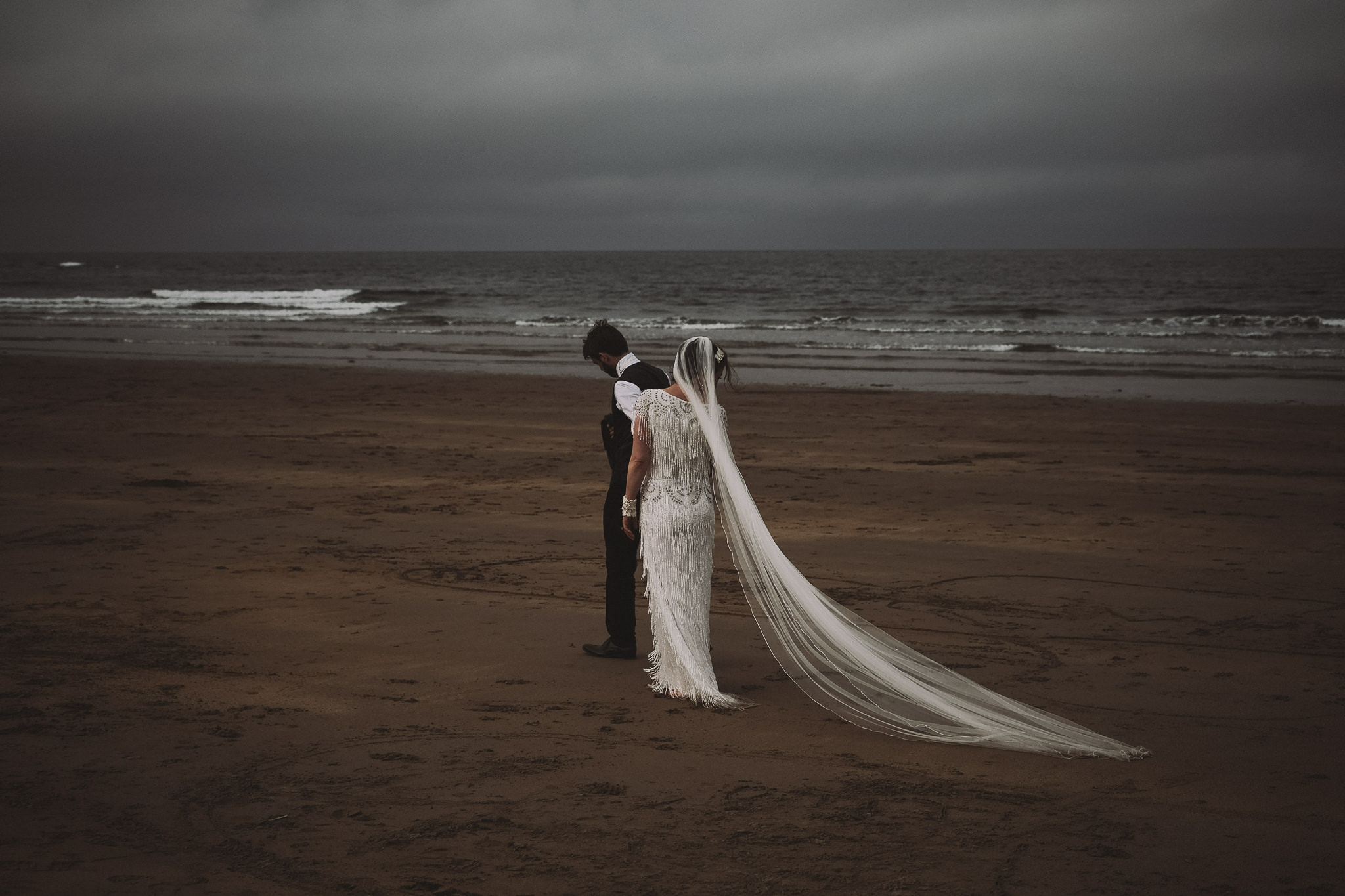Bride and groom walk along a stormy beach in Northumberland