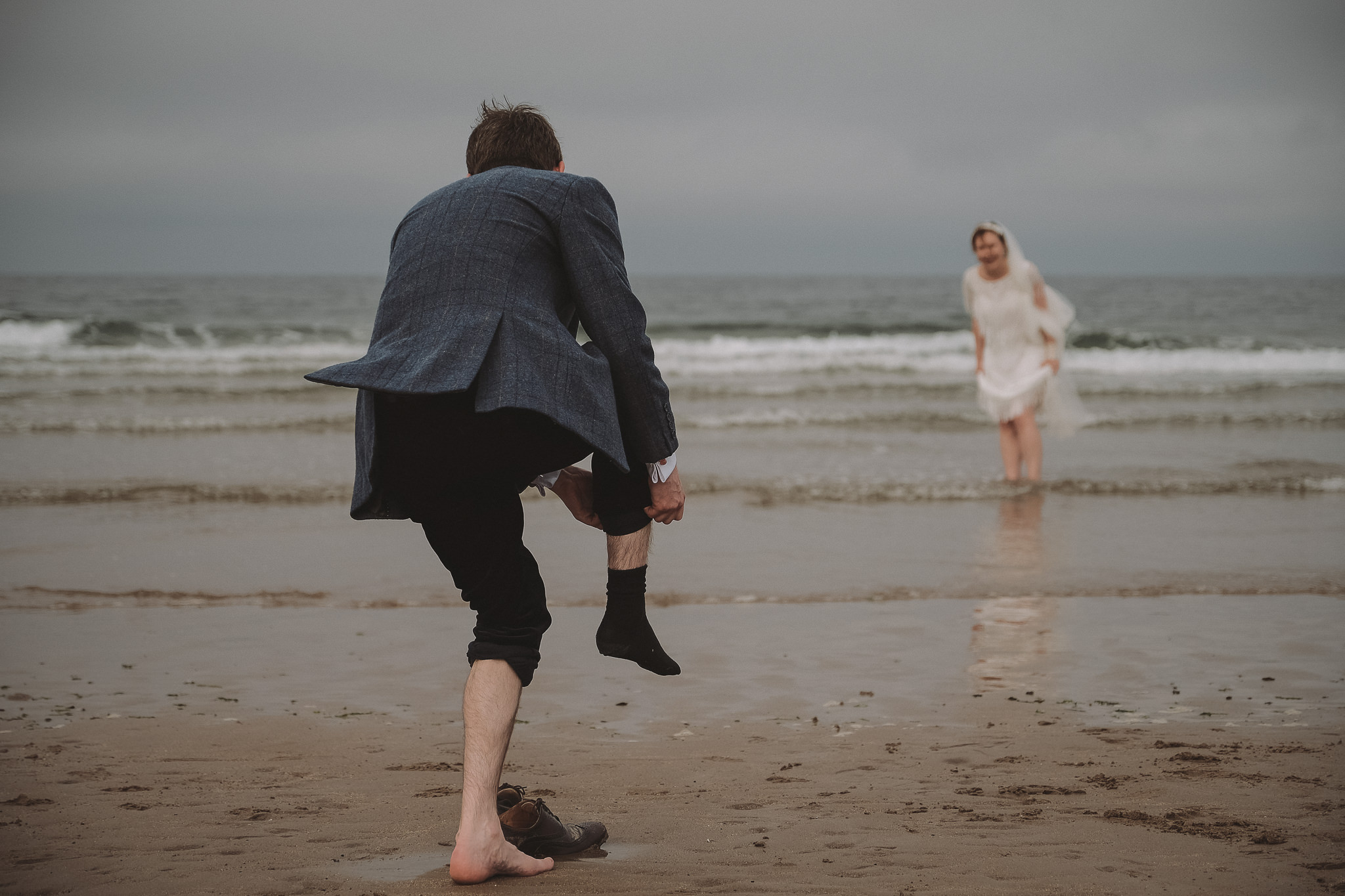 Groom takes off his socks to join his bride in the sea on the Northumberland coast