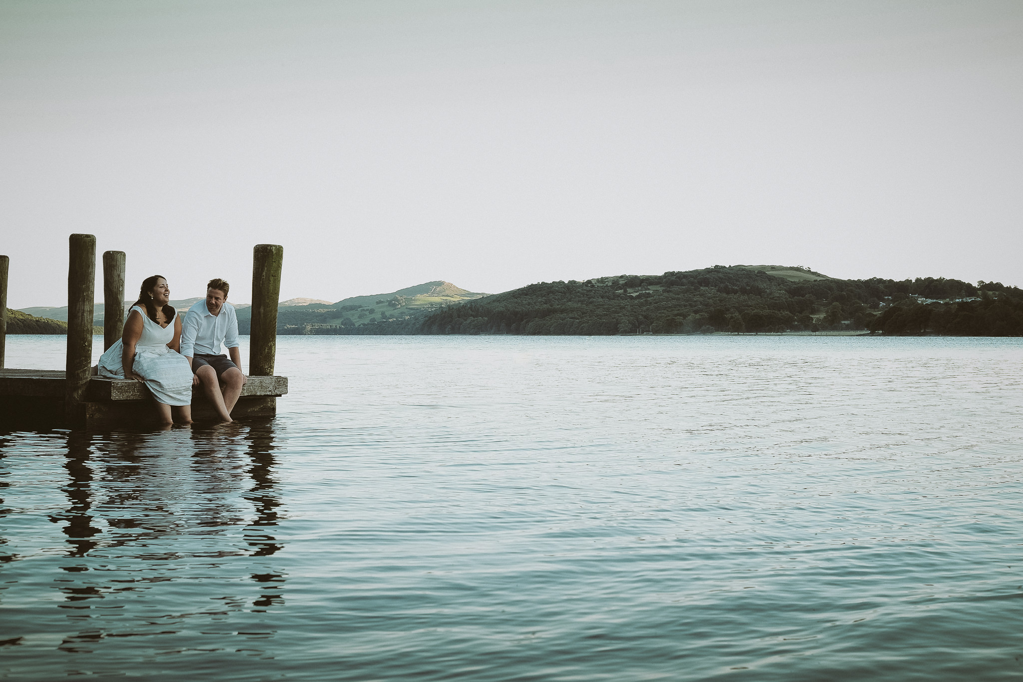 Bride and groom sit on a jetty on Coniston Lake
