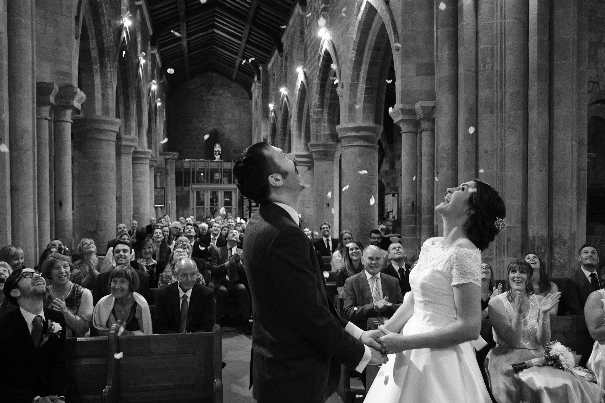 Black and white photo of the bride and groom being showered with confetti in the church