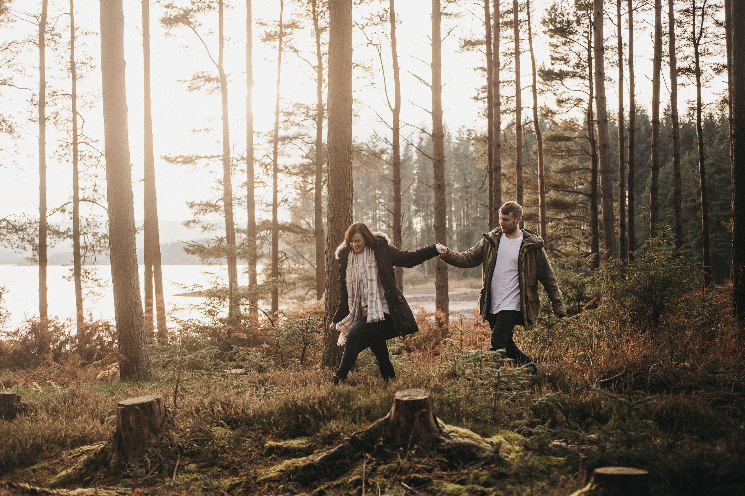 Couple hold hands while picking their way through undergrowth in Kielder Forest