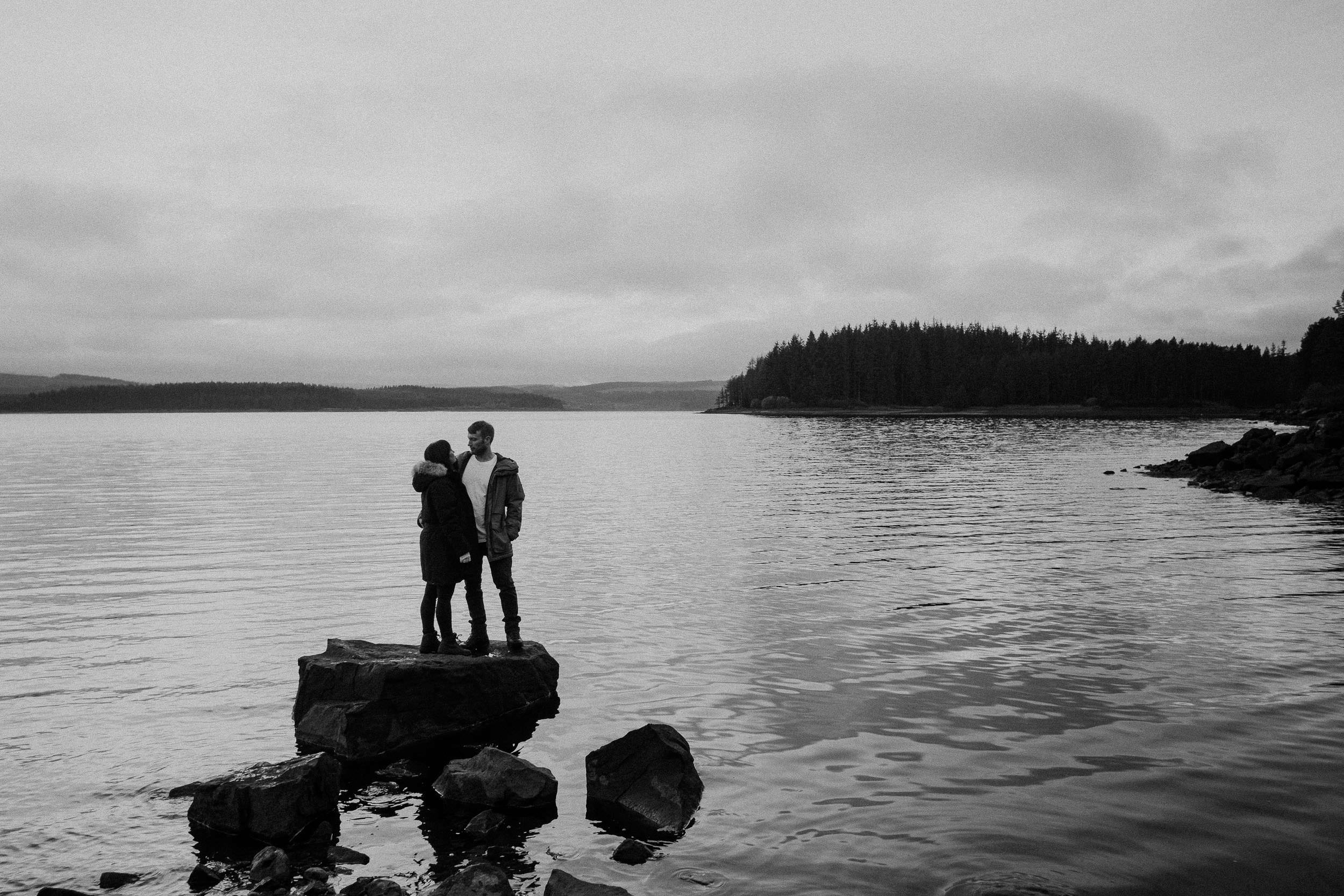 Black and white photo of a couple standing on a rock in Kielder water