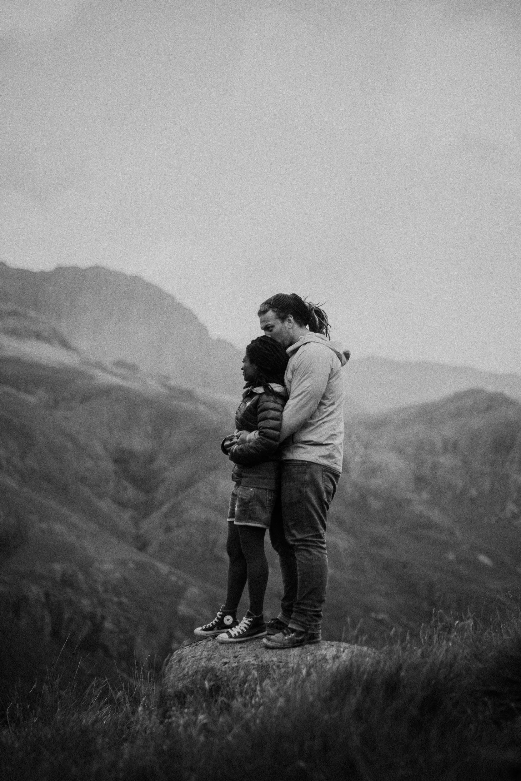 Black and white photo of pre-wedding couple cuddling on rock