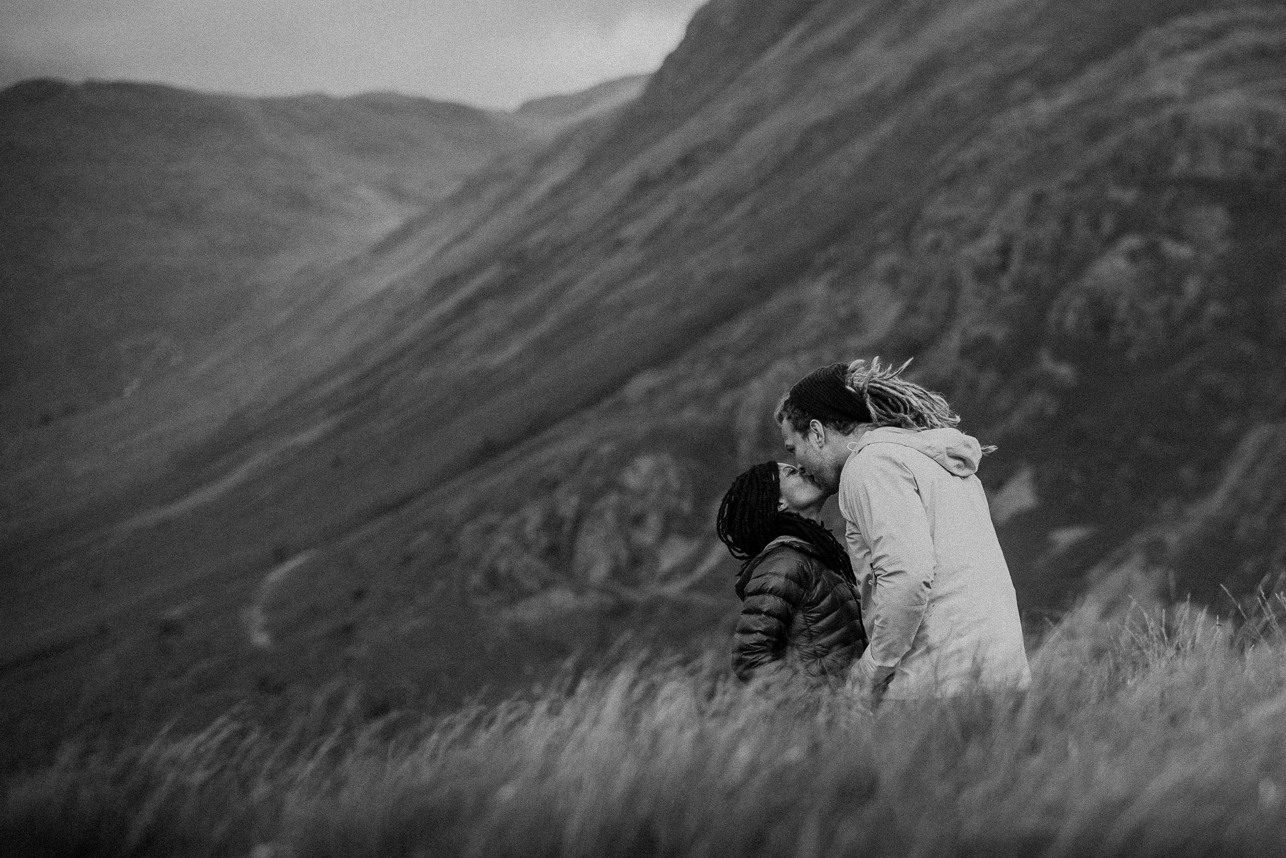 Black and white photo of engaged couple kissing on Lake District hillside