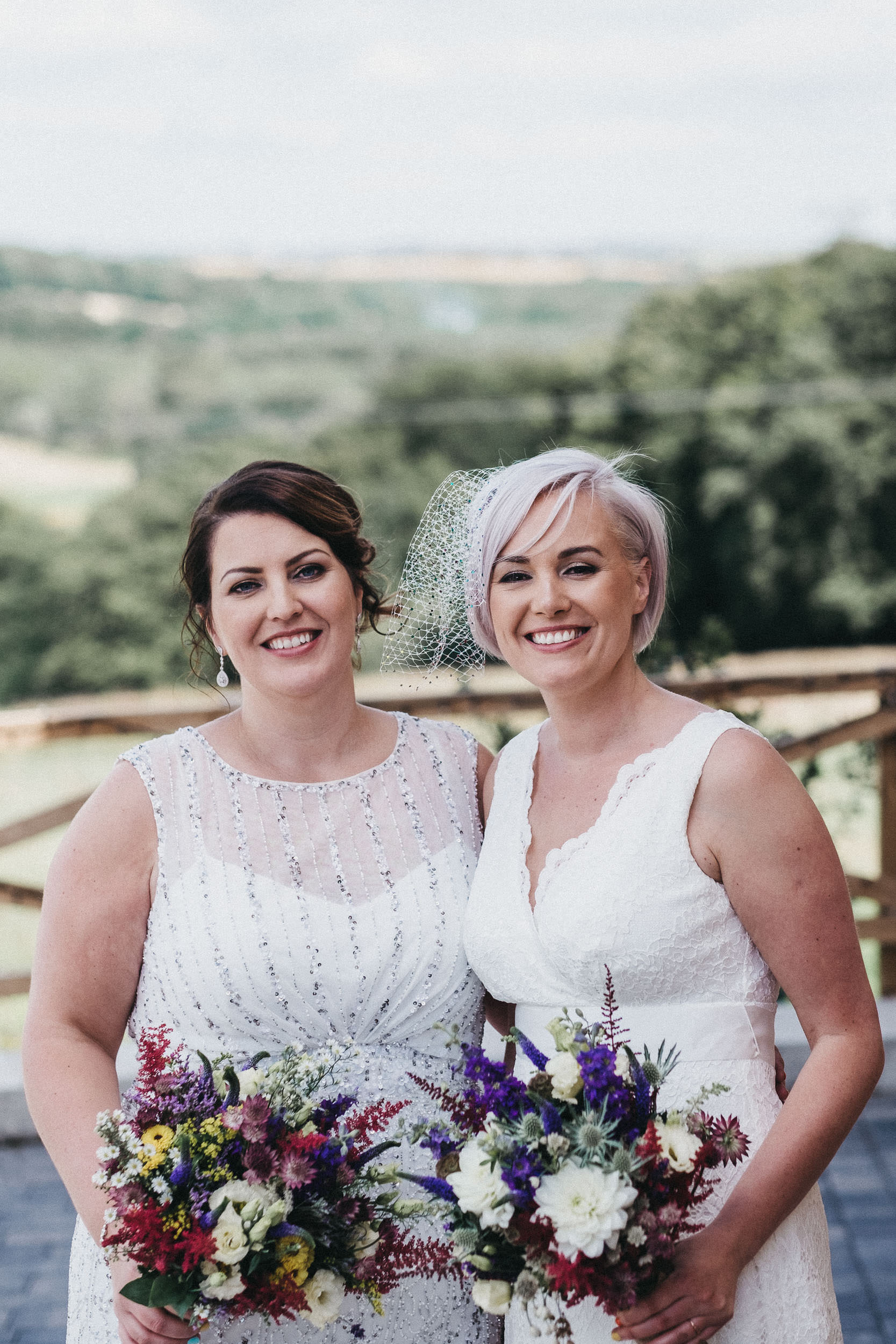 Two brides smiling while holding bouquets at same sex wedding