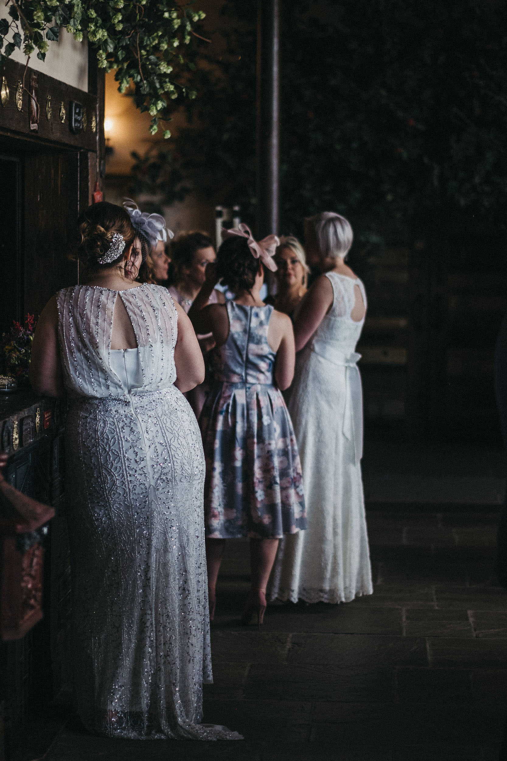 One bride watches the other bride while leaning against bar