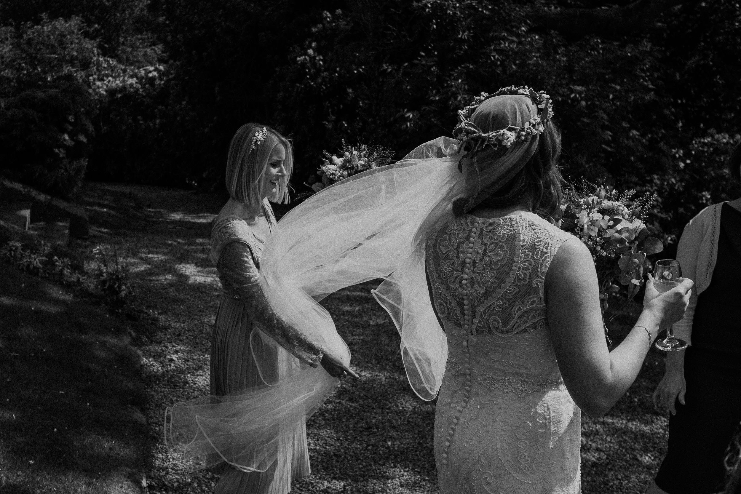 Black and white photo of bridesmaid holding bride's veil in wind