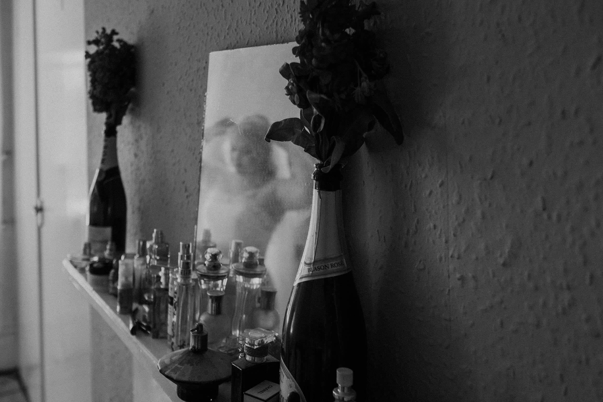 Black and white photo of champagne bottles filled with roses with reflection of bride in mirror