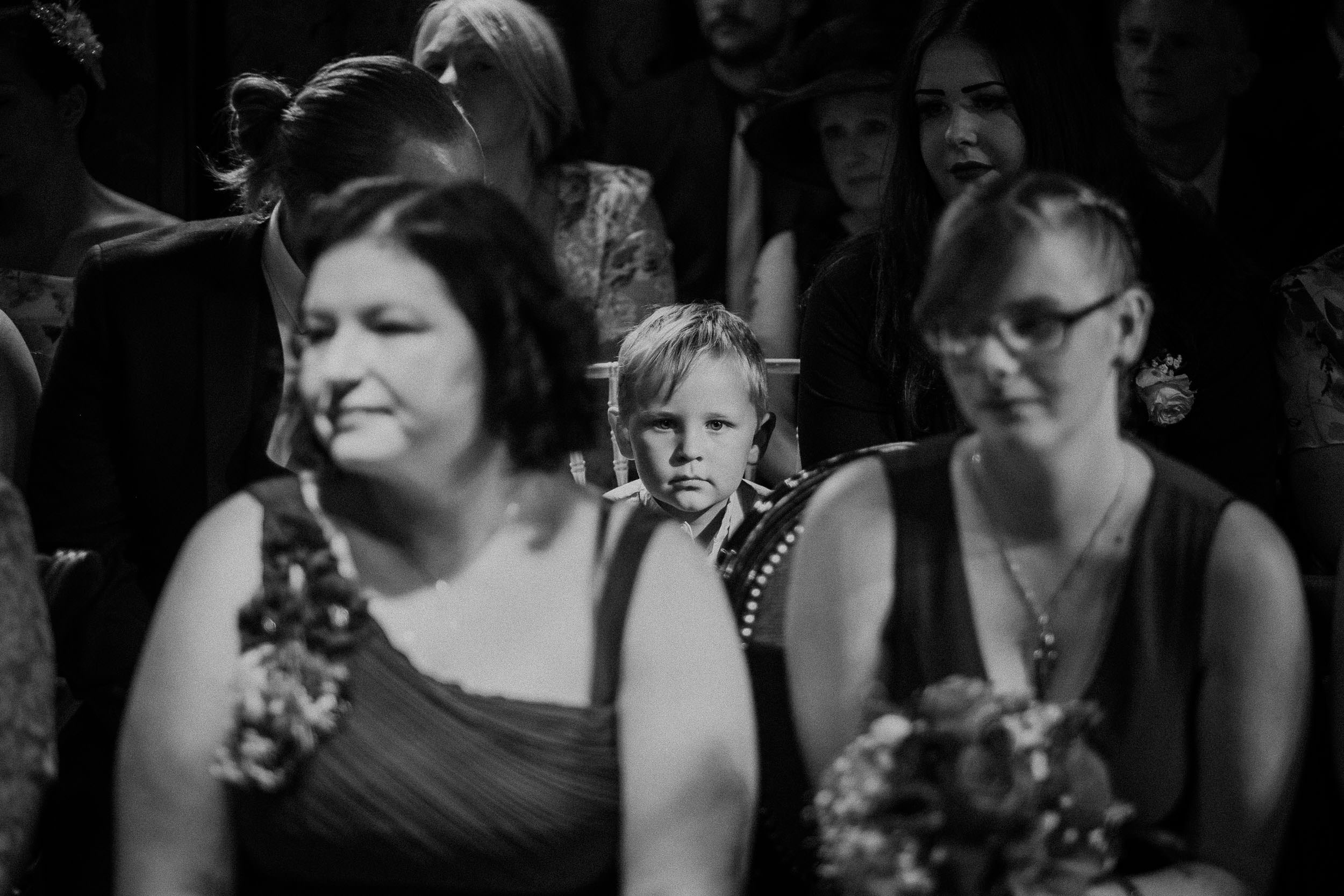 Black and white photo of child looking at camera during wedding ceremony