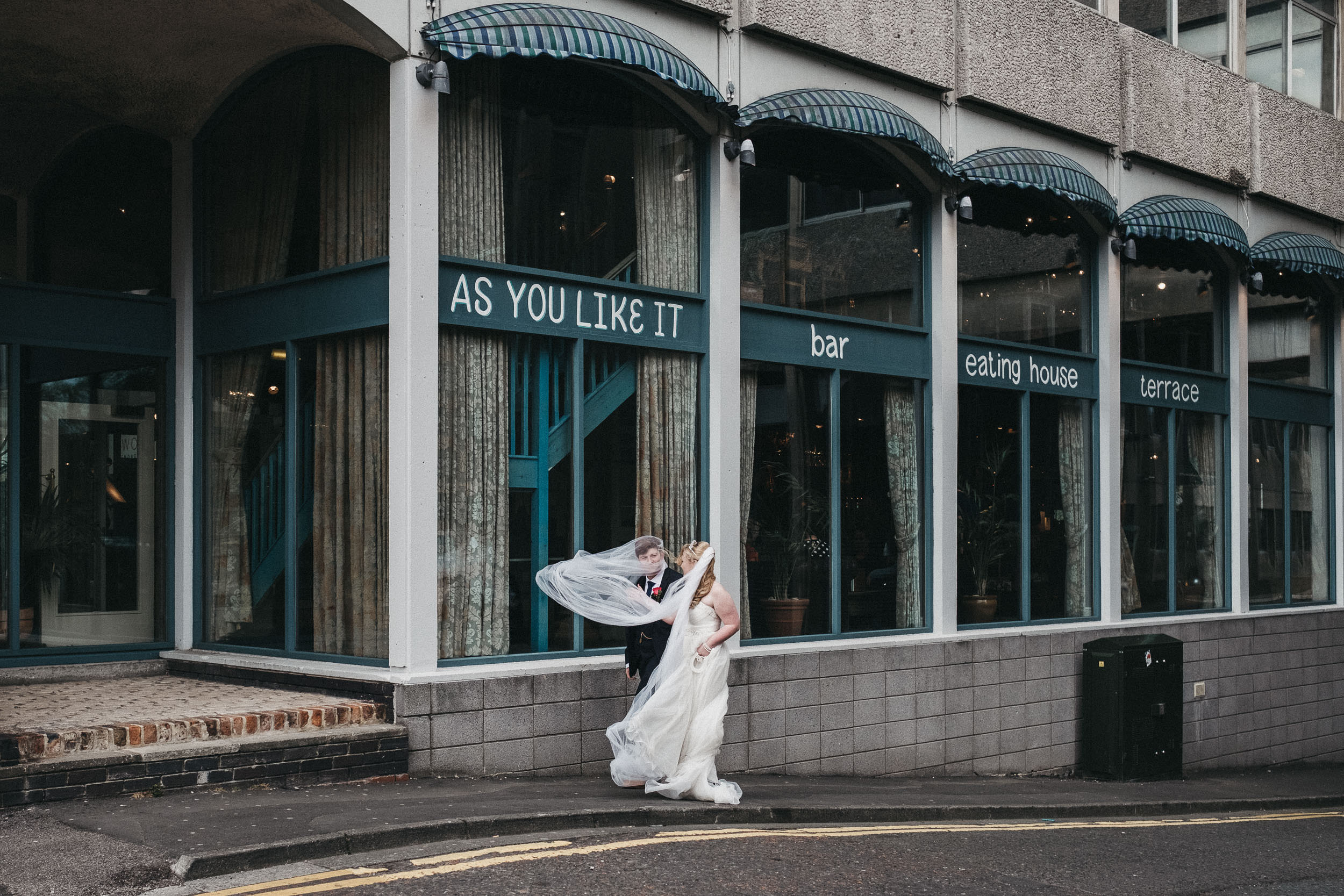 Bride and groom outside As You Like It with veil blowing on groom's head