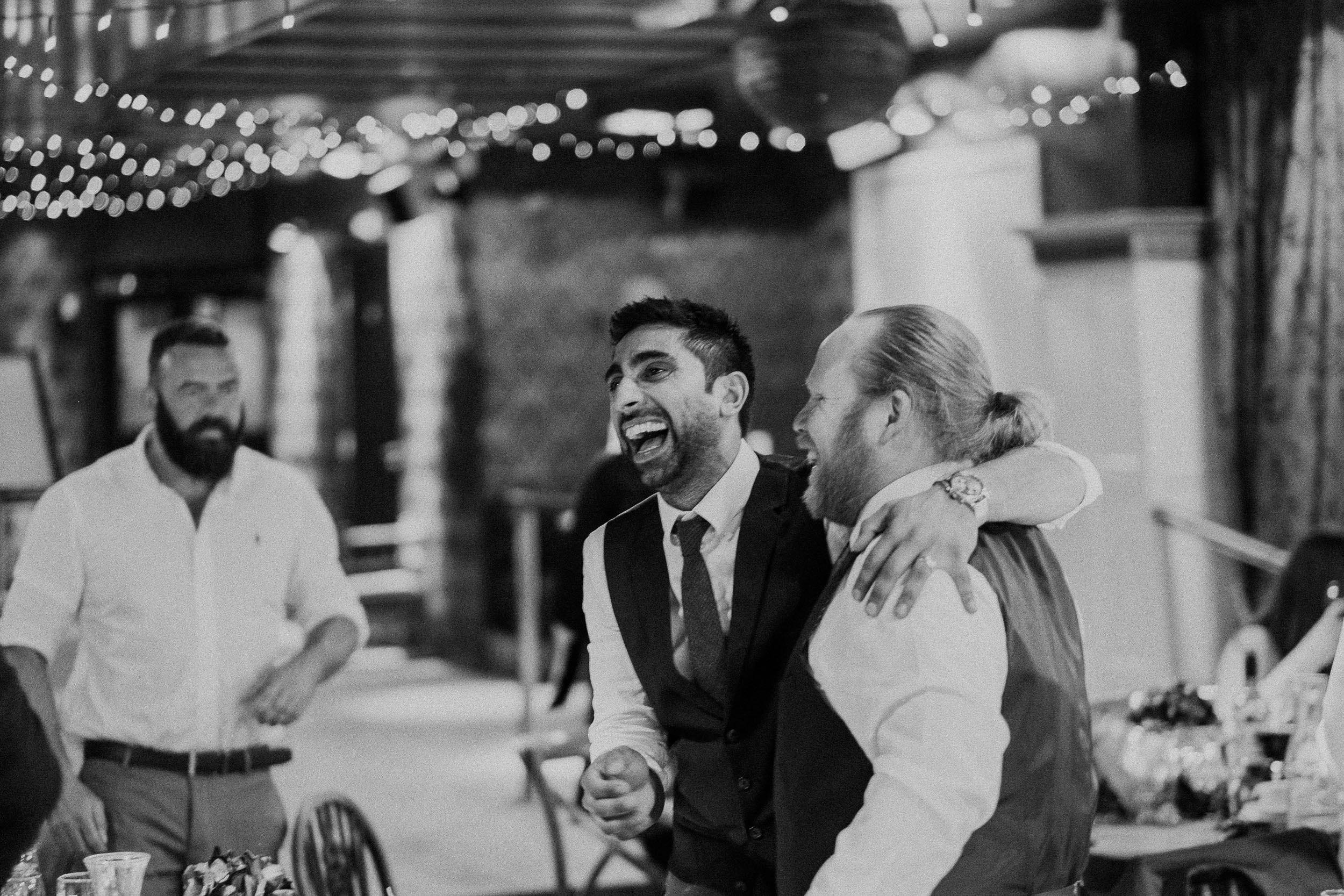 Black and white photo of wedding guests roaring with laughter after speeches