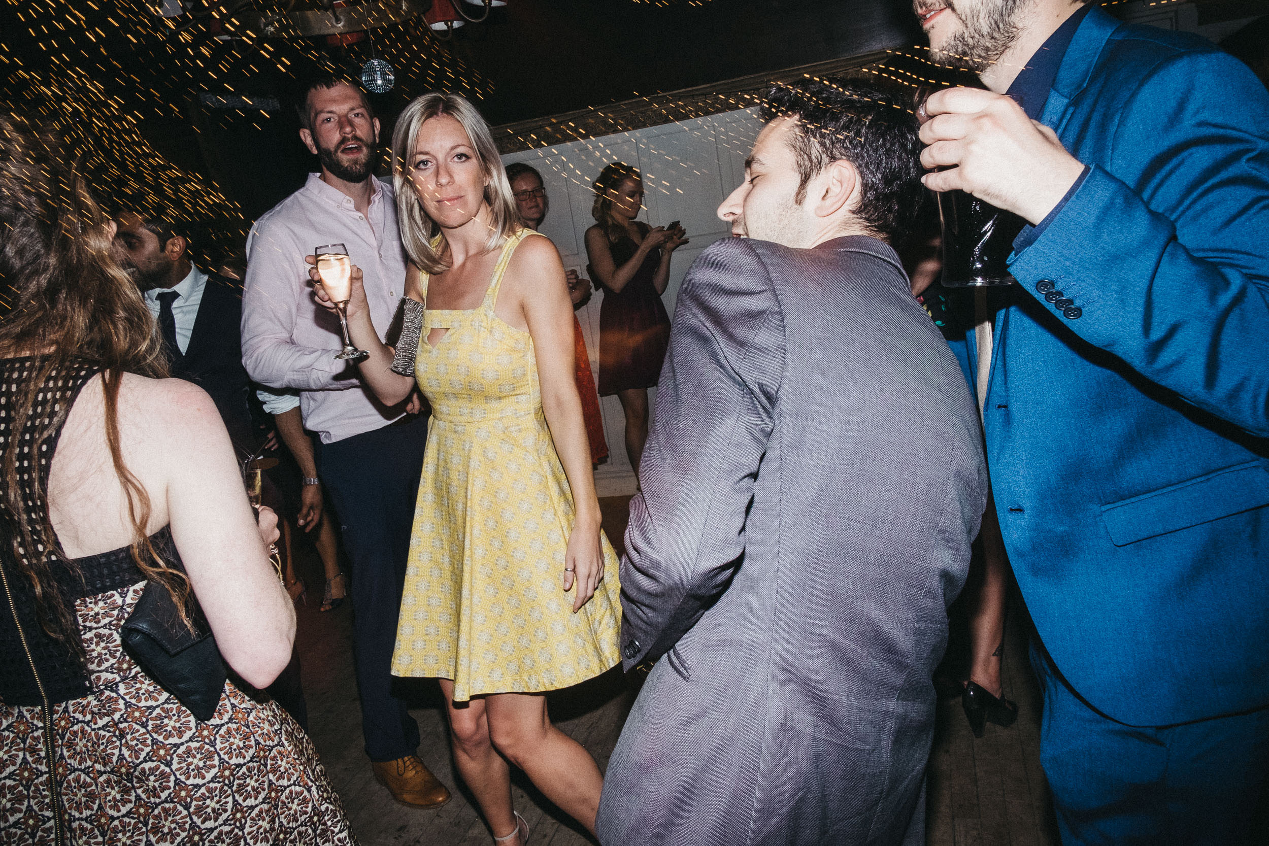 Wedding guest walks through busy wedding dance floor carrying wine glass