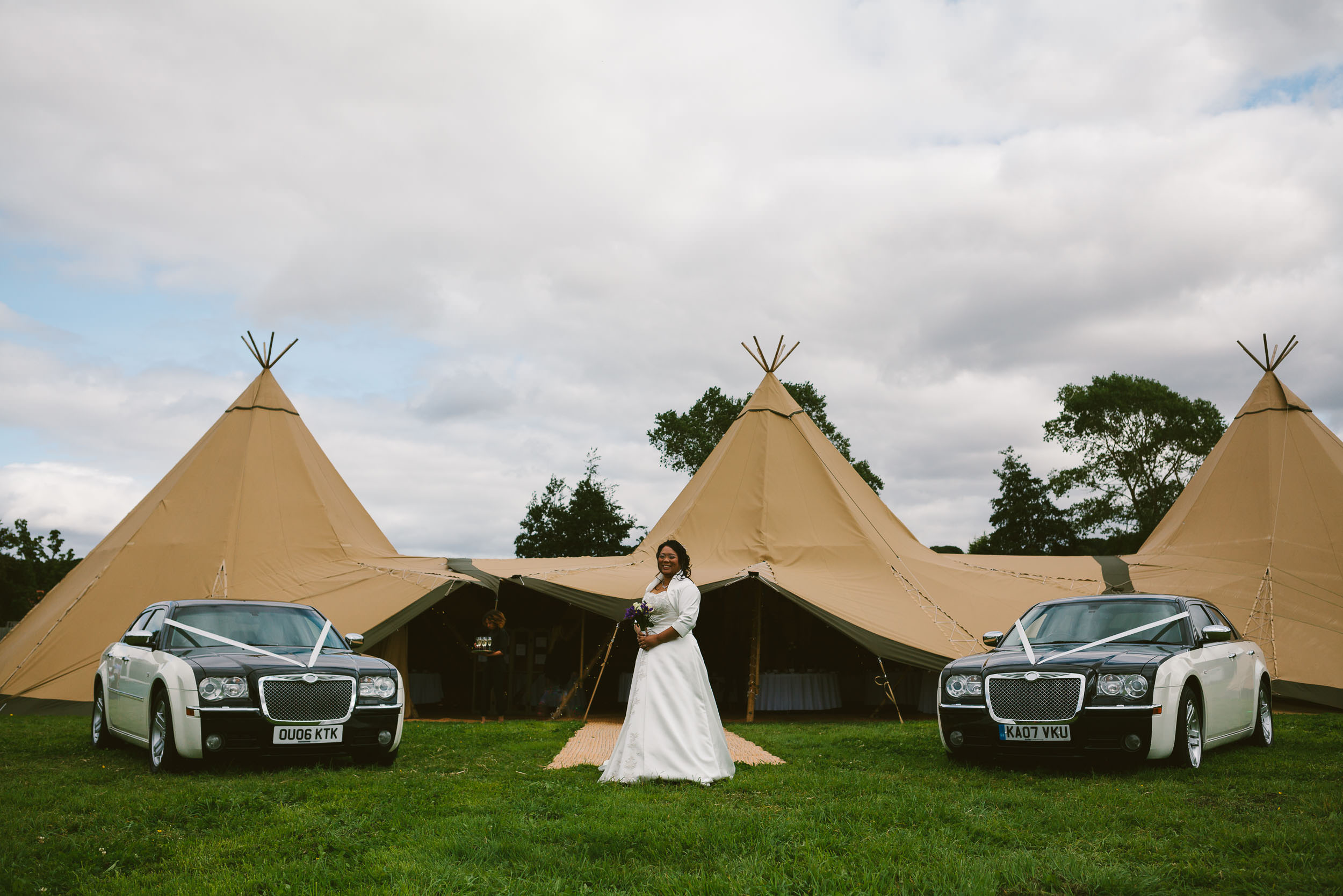 Bride poses between two Bentleys with Tipi in background