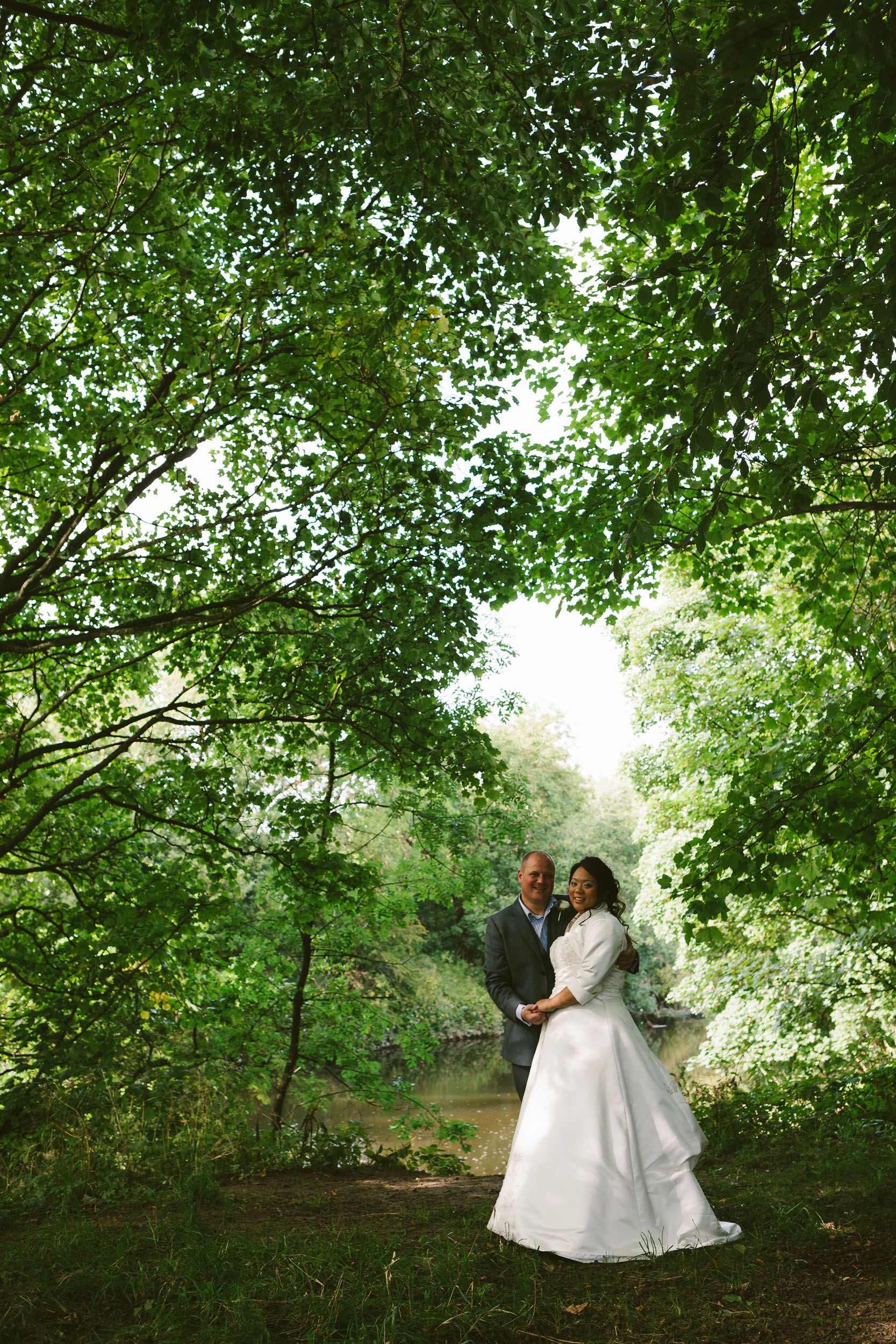 Bride and groom pose under canopy of green trees